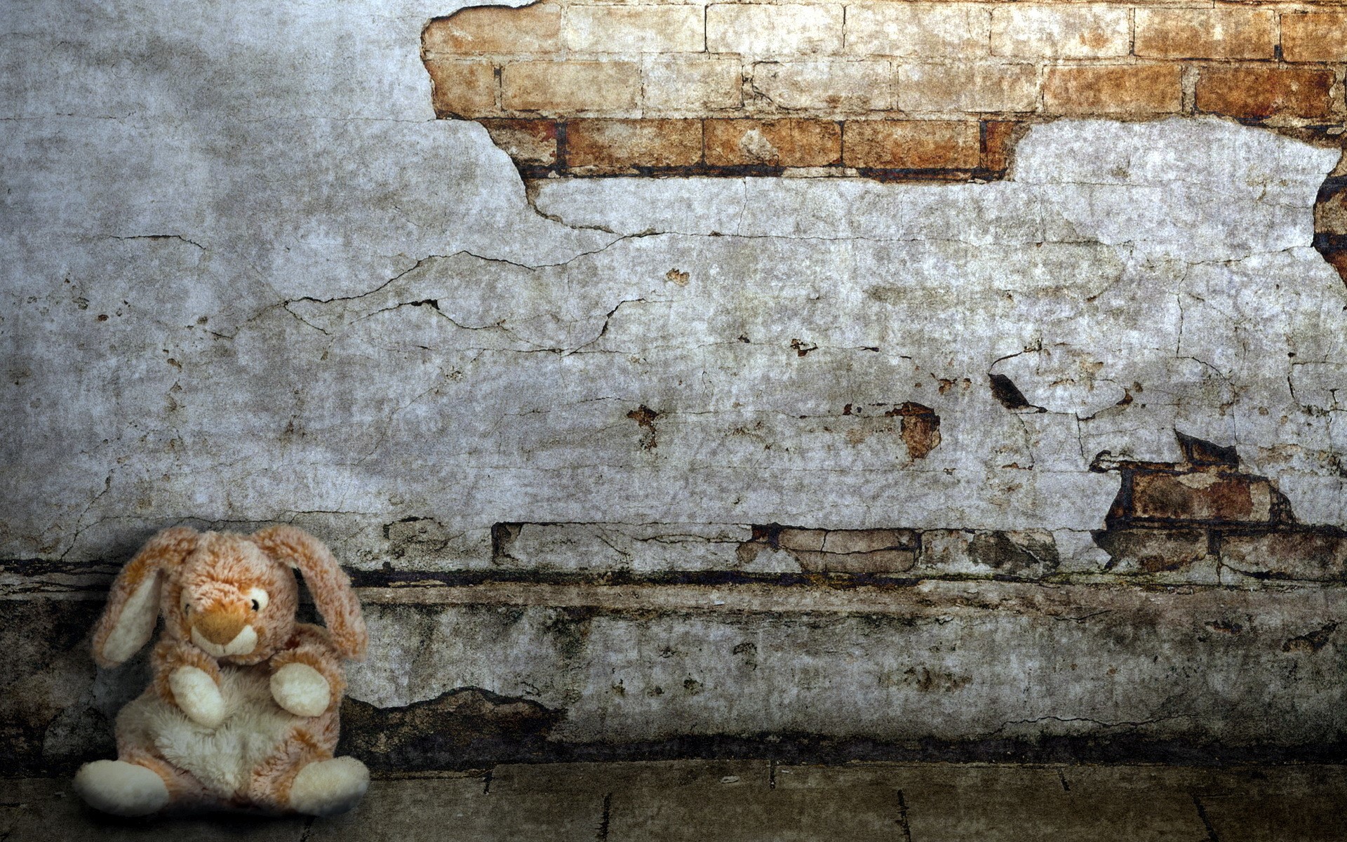 A lone stuffed bunny sits against a decaying brick wall HD Wallpaper