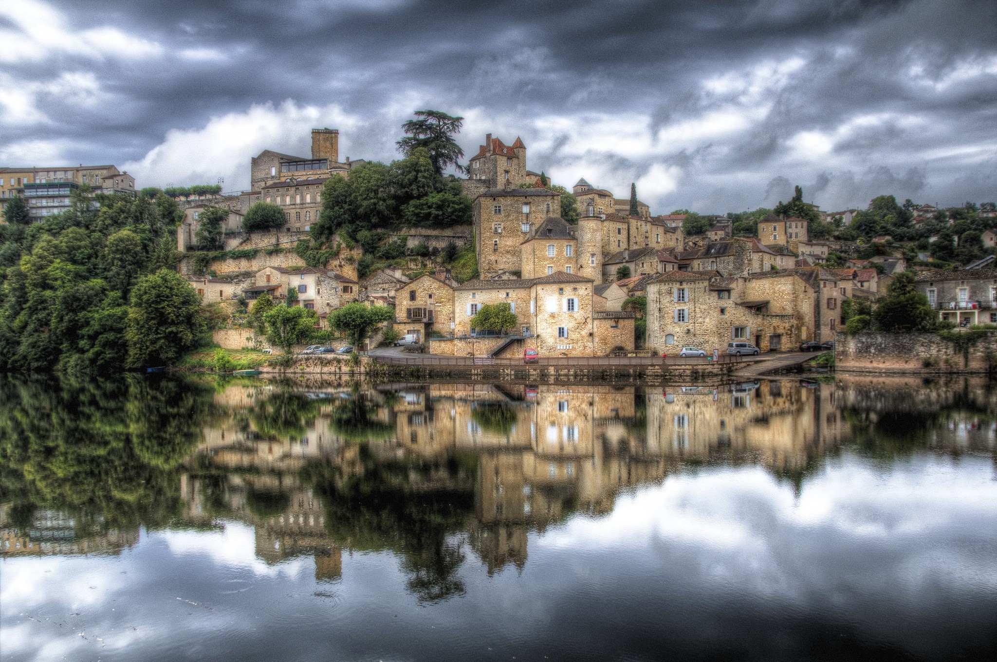 Puy l'Eveque village reflected in a river under a cloudy sky HD Wallpaper