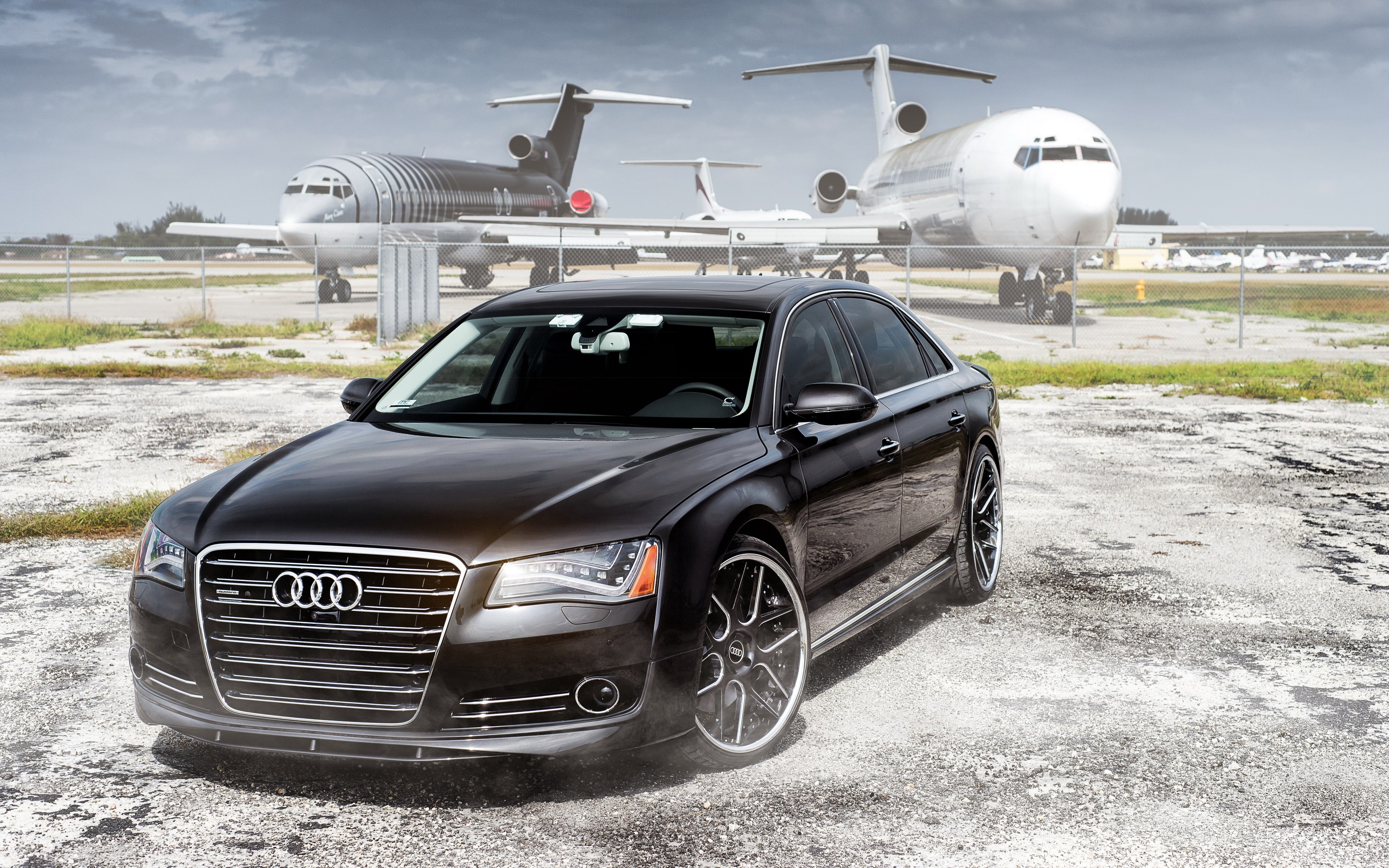 Black Audi A8 parked at an airport with airplanes HD Wallpaper