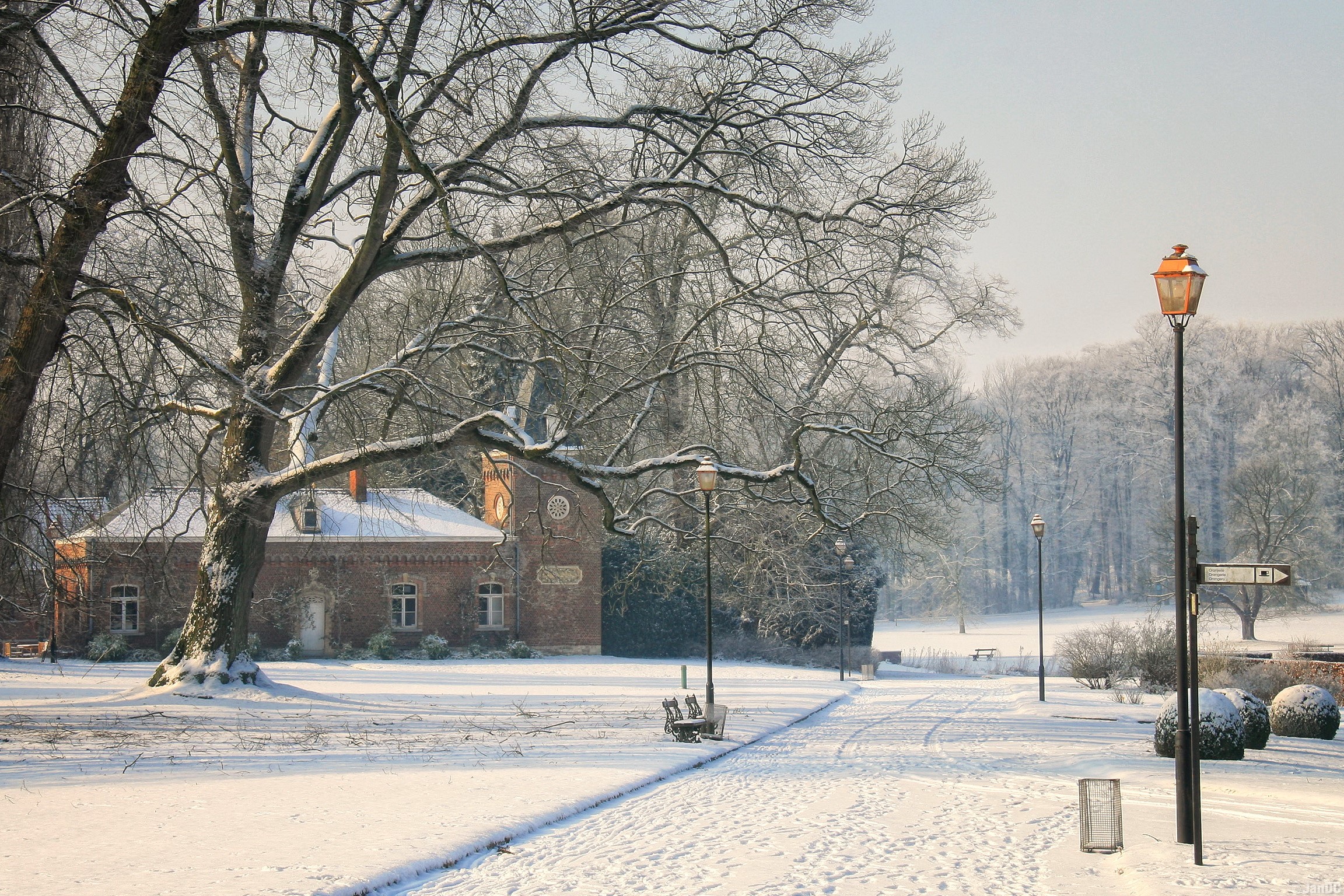 Winter scene in Meise, Belgium with a brick building and snow-covered trees HD Wallpaper