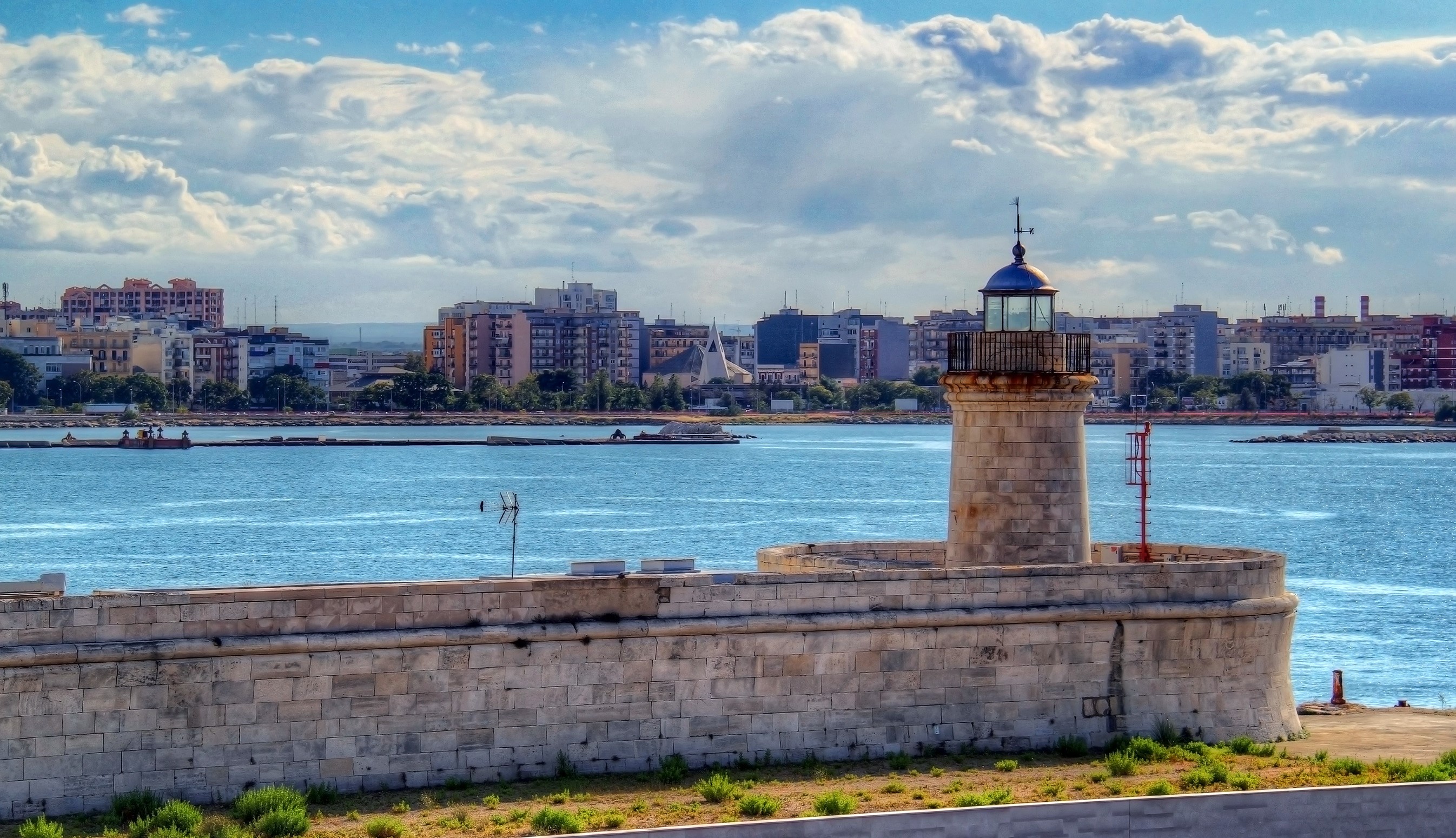 Lighthouse on stone pier with city skyline in Apulia, Italy HD Wallpaper