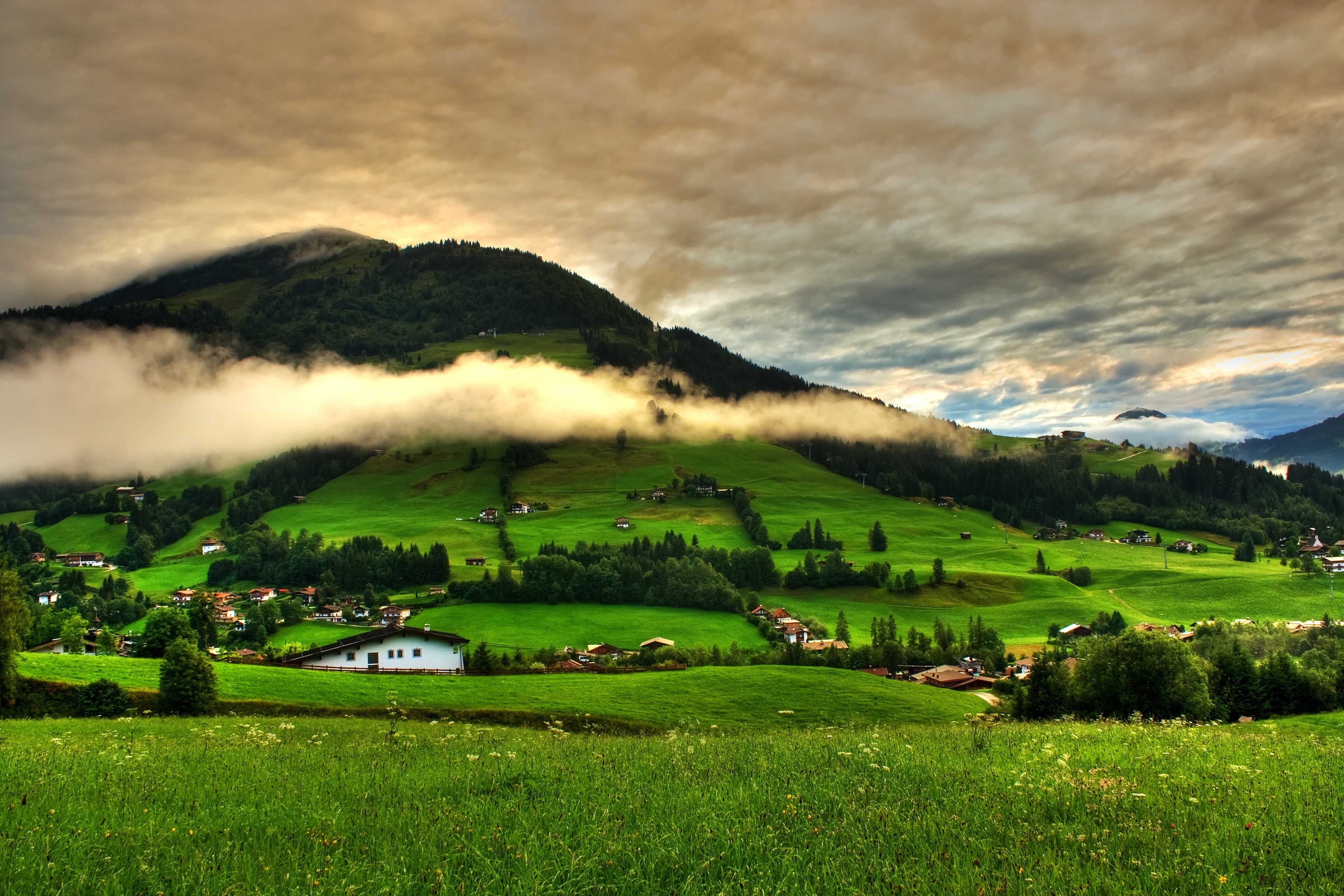 Green Mountainside Village with Foggy Clouds HD Wallpaper