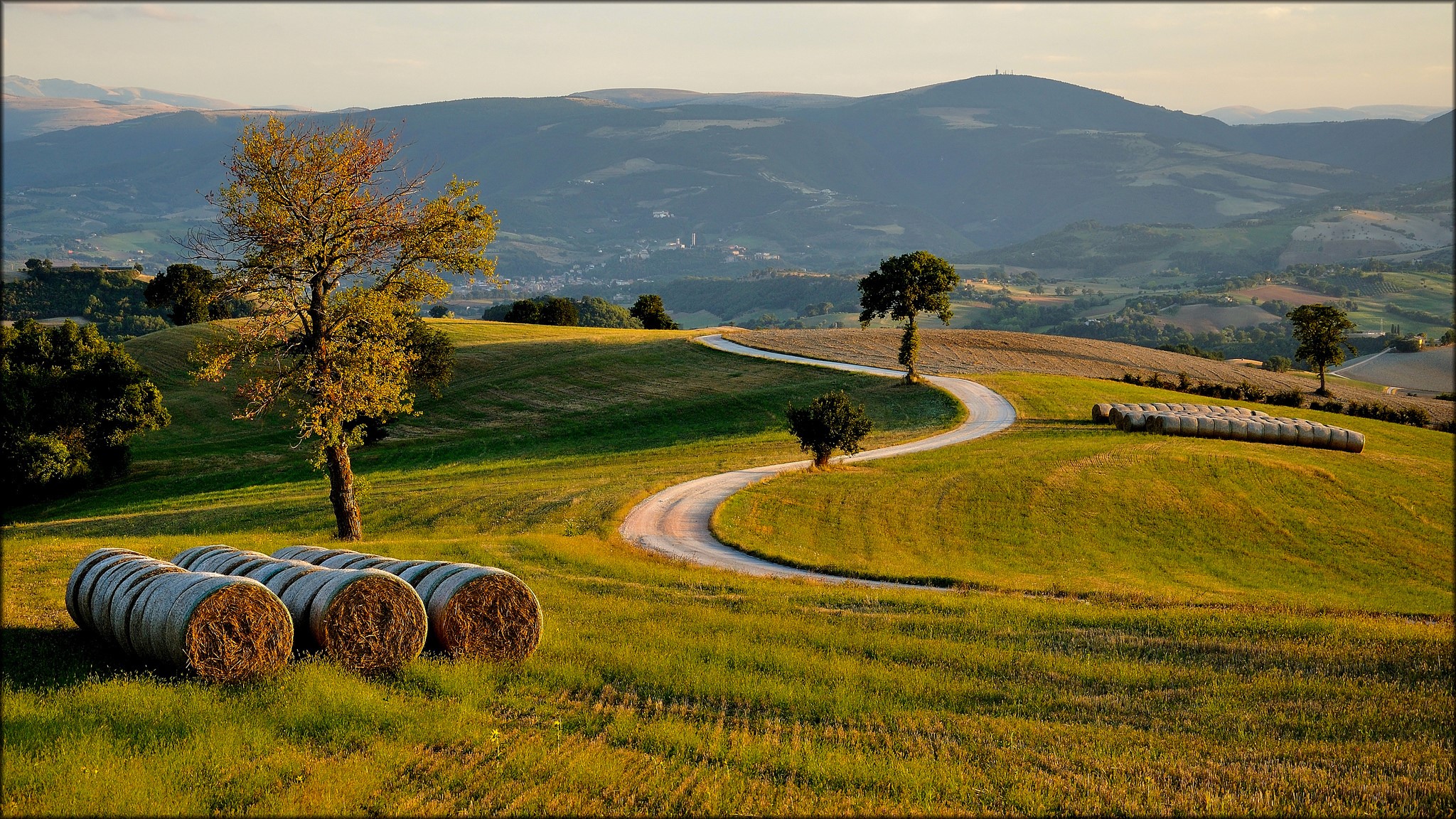Rolling Hills with Hay Bales and Winding Road in Italy HD Wallpaper
