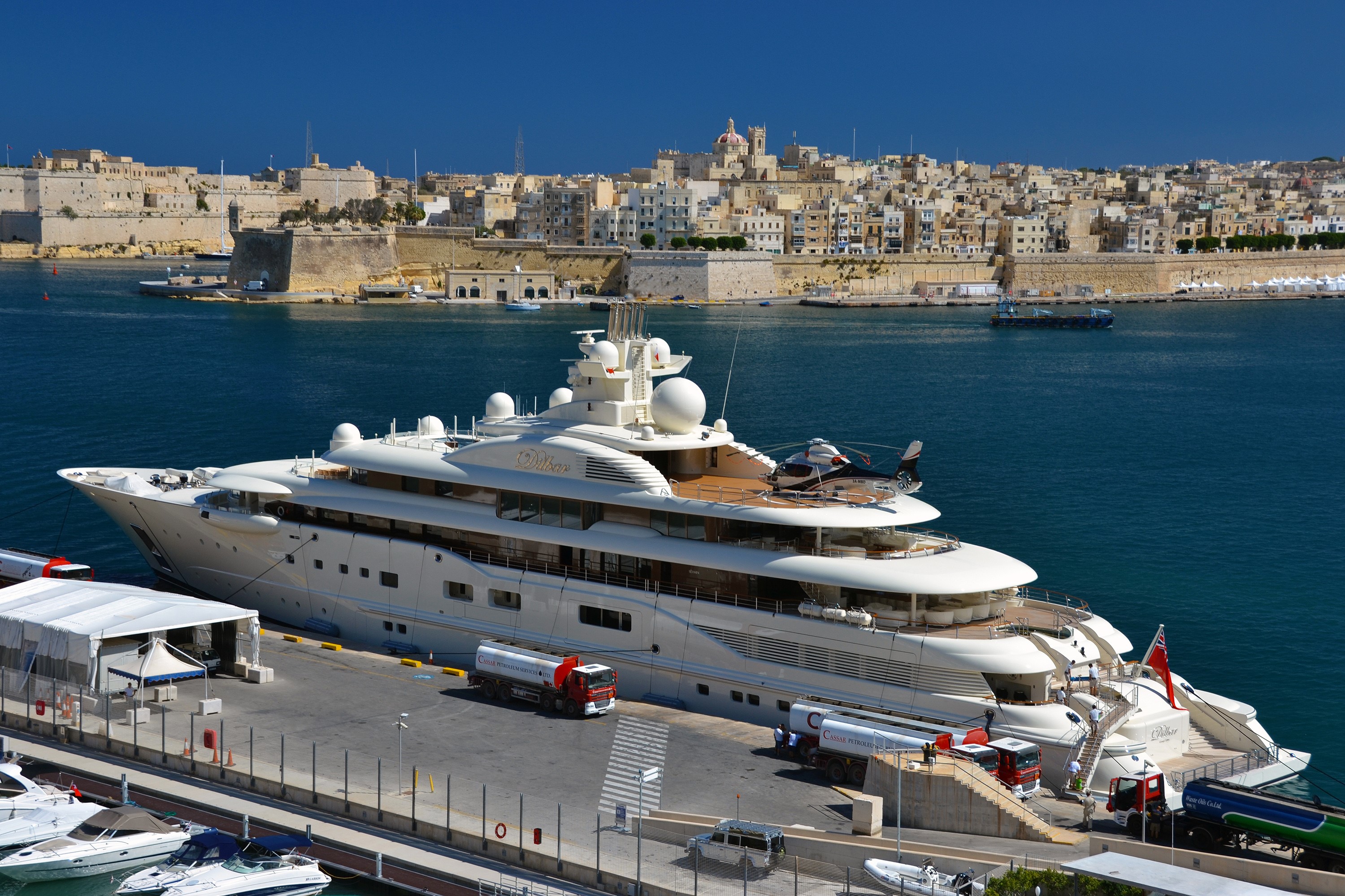 Luxury yacht docked in a harbor with a historic city in the background HD Wallpaper