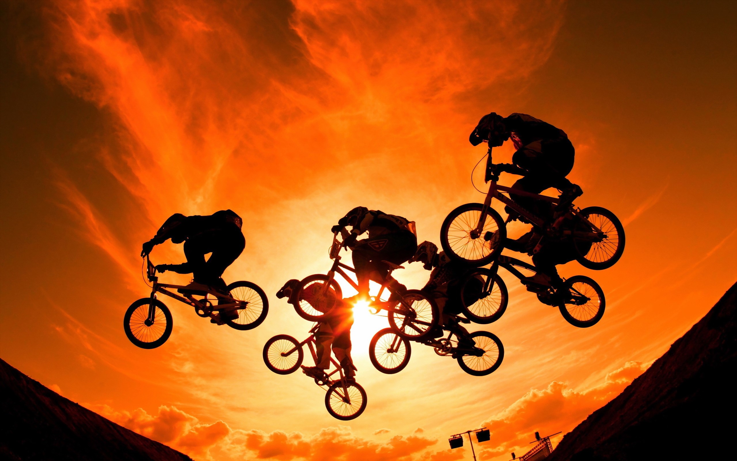 BMX riders performing jumps against a sunset sky HD Wallpaper