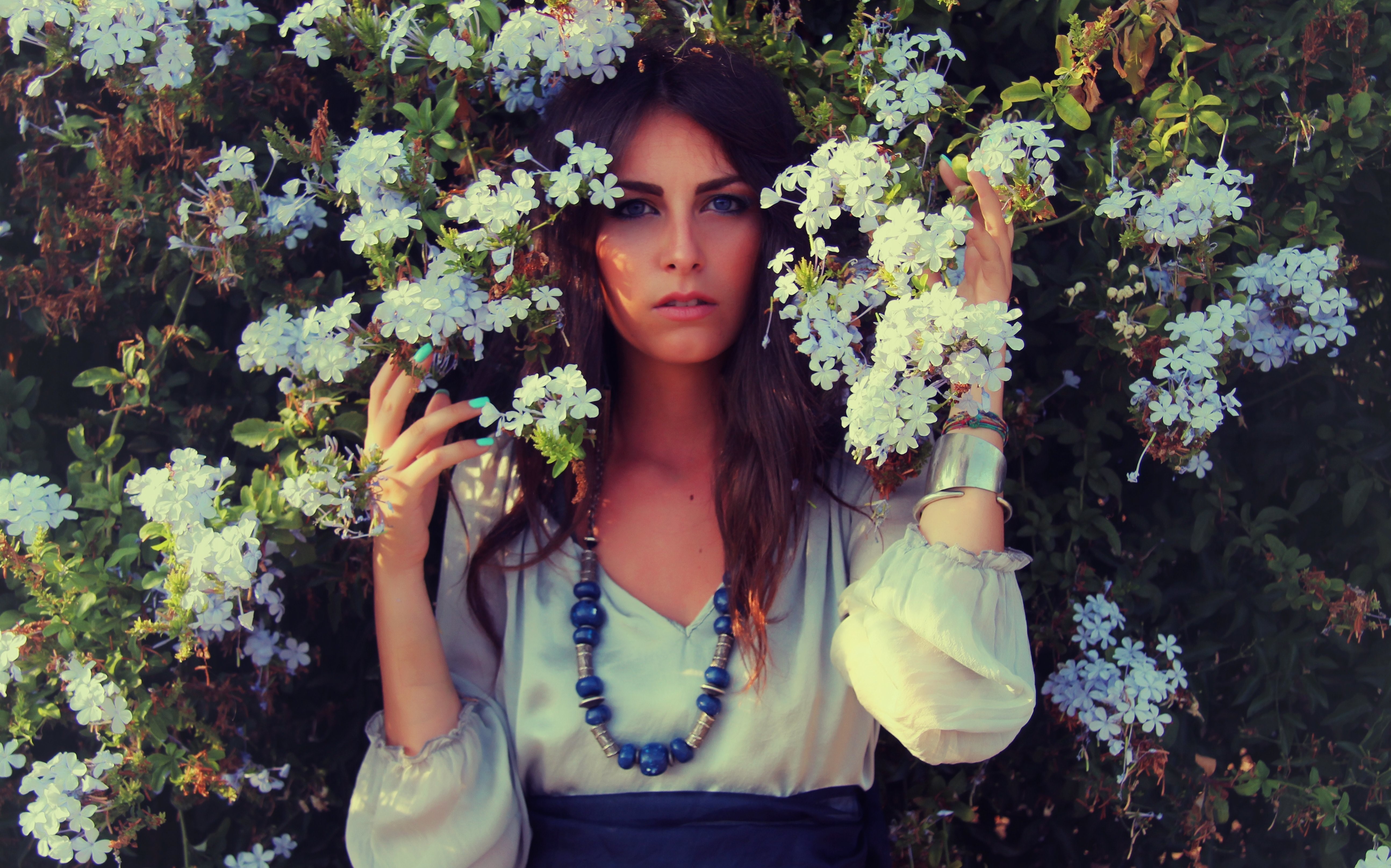 Woman with brown hair and blue eyes surrounded by white flowers HD Wallpaper