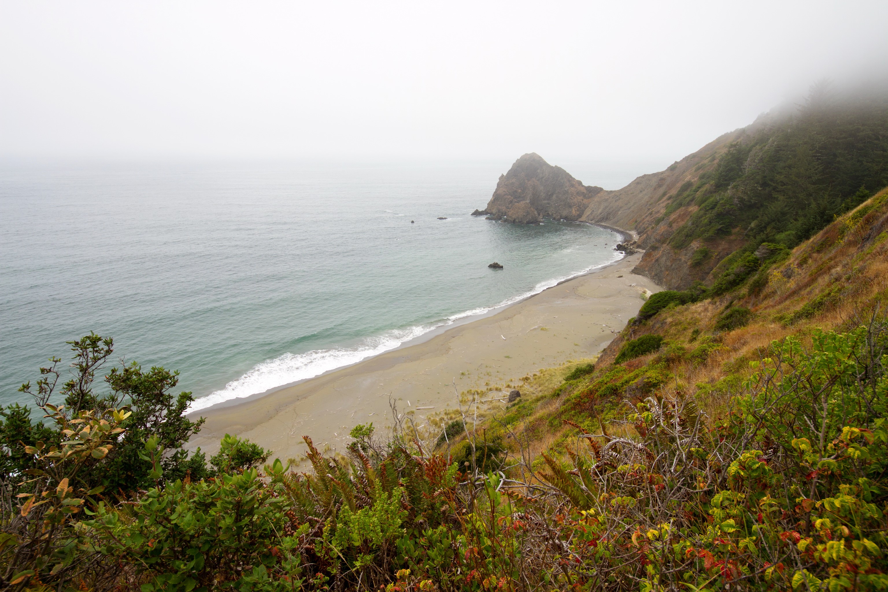 Misty Coastline with Beach and Rocky Outcrop HD Wallpaper