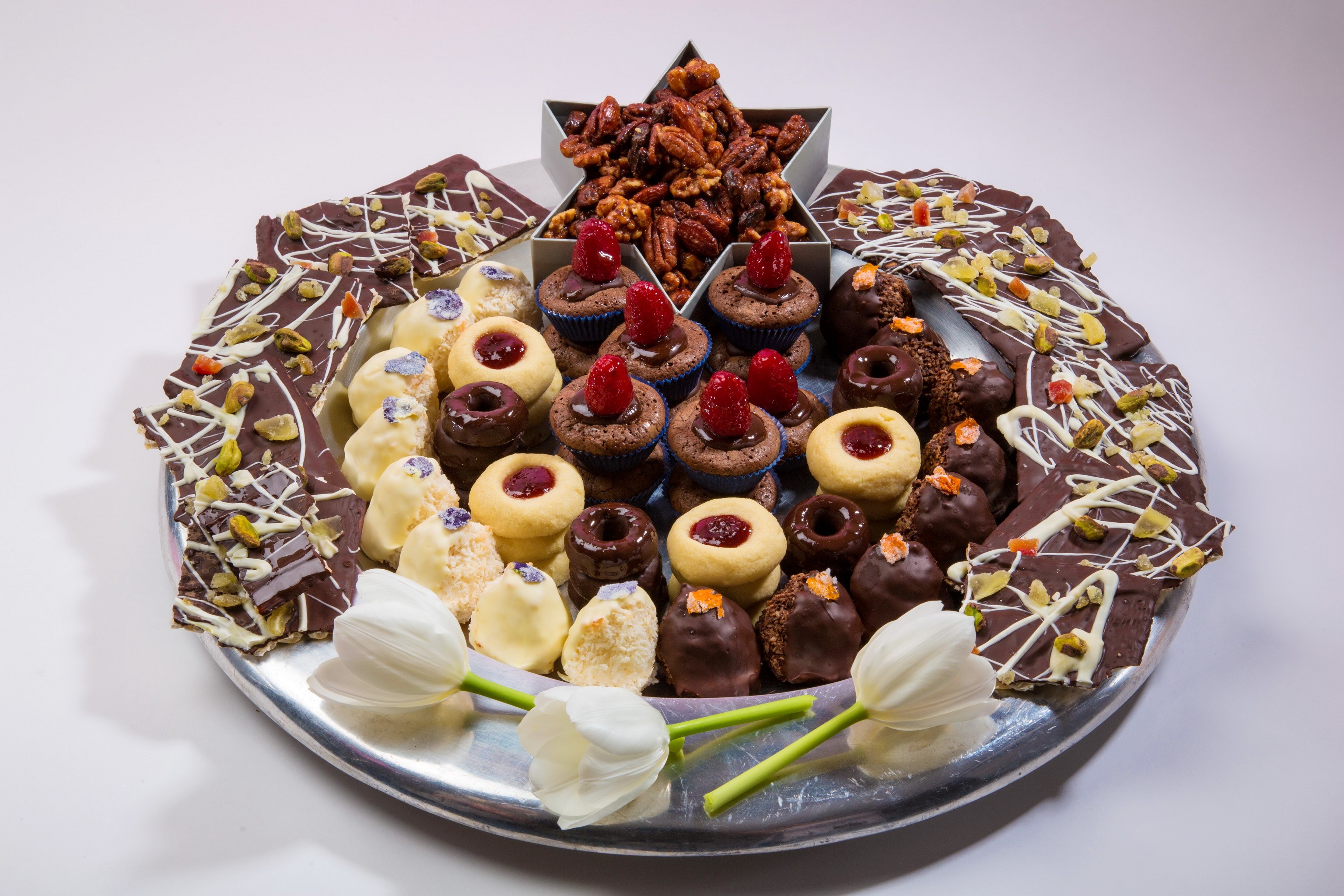 Assortment of chocolates, cupcakes, and nuts on a silver platter with tulips HD Wallpaper