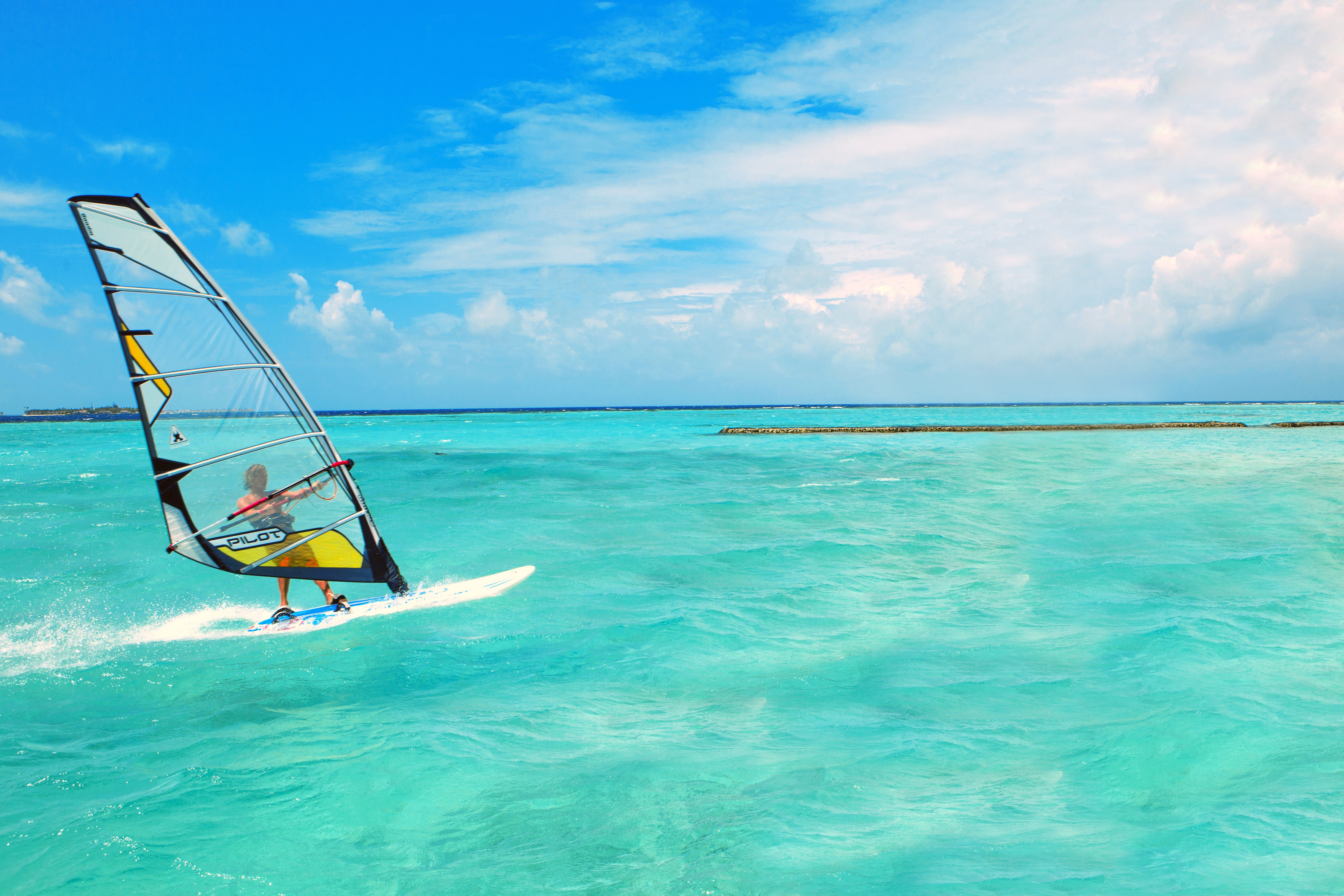Windsurfing on a turquoise sea under a cloudy sky HD Wallpaper