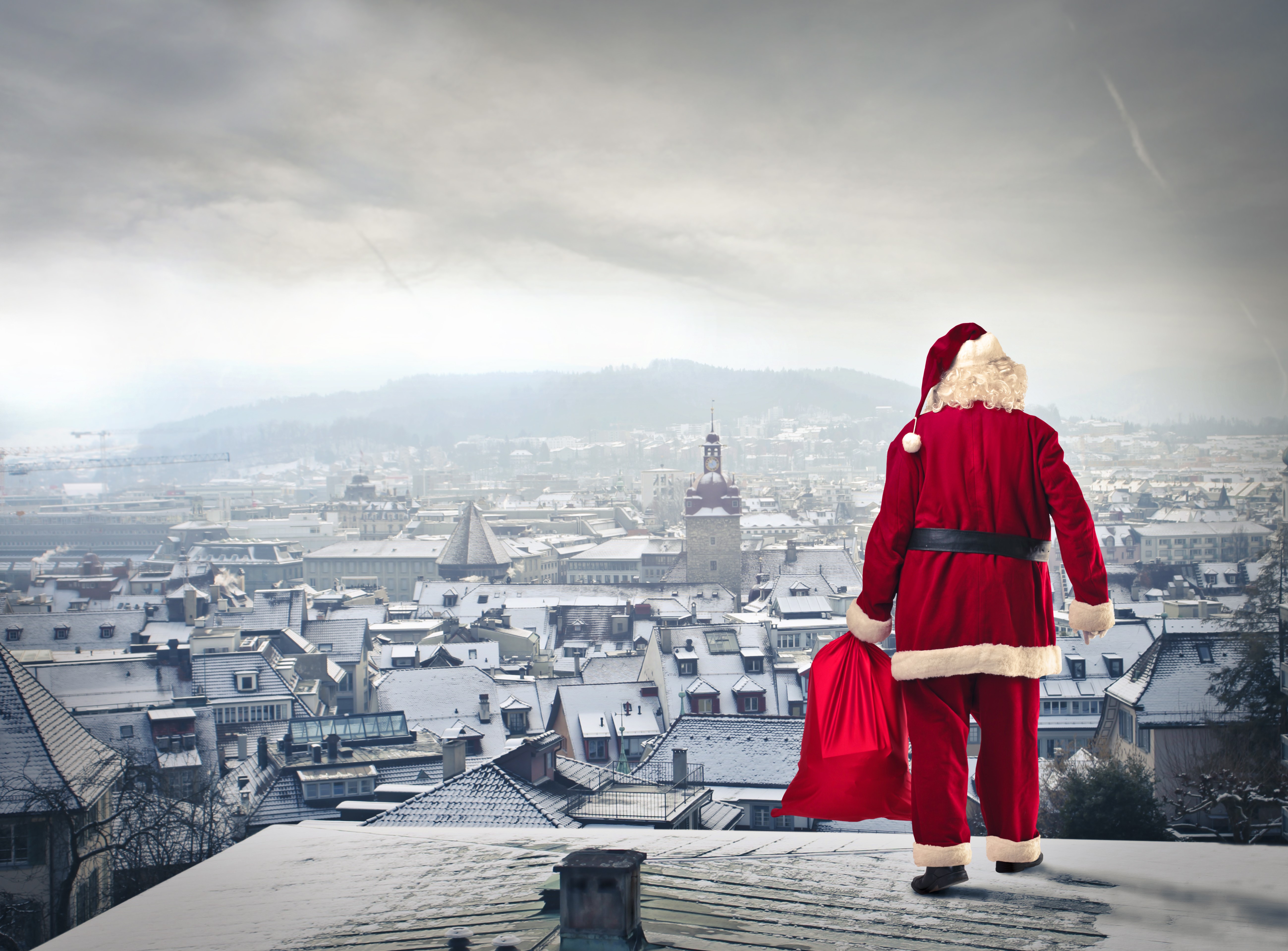 Santa Claus with a gift bag overlooking a snowy city HD Wallpaper