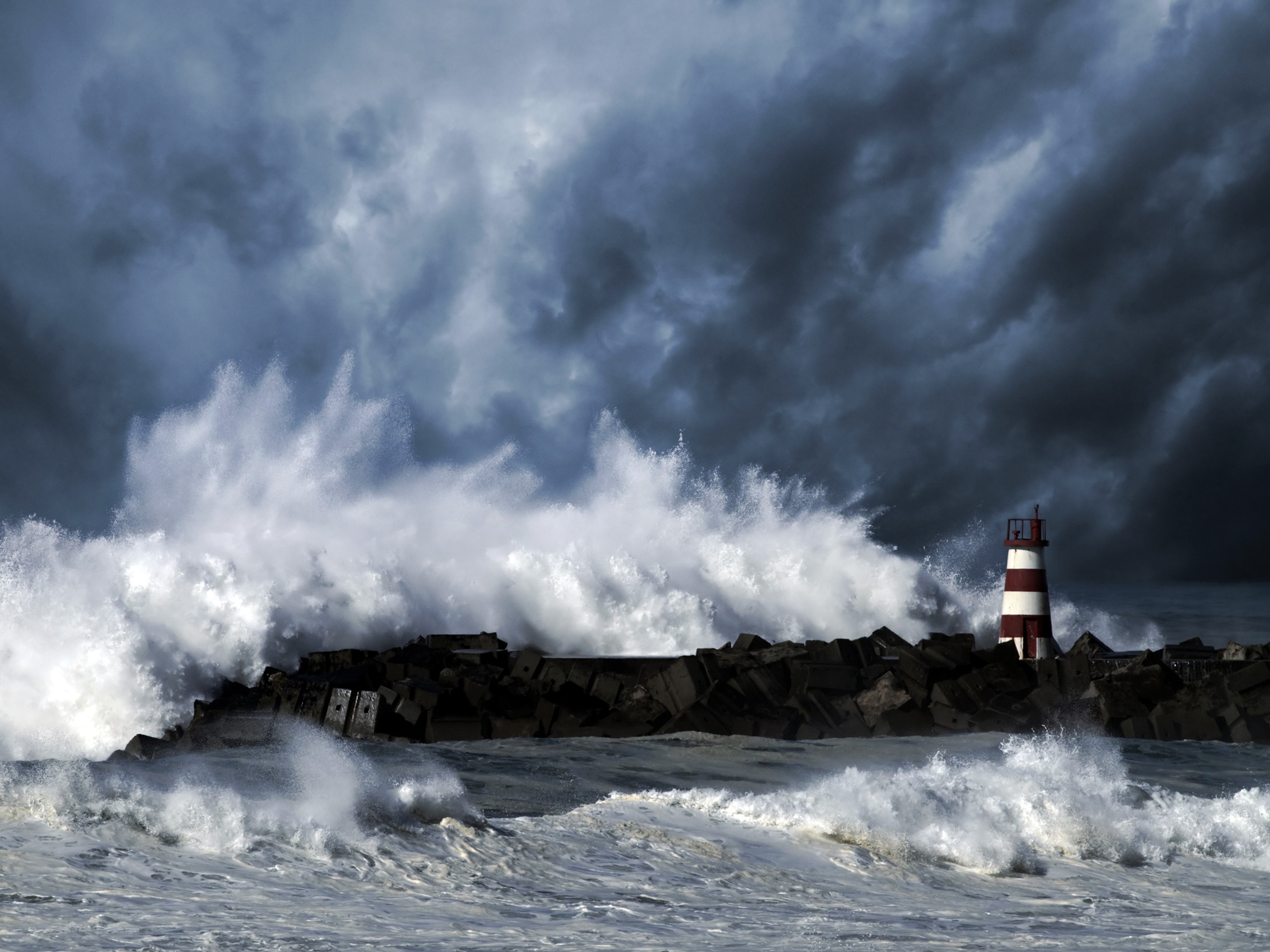 Stormy seas crash against a lighthouse on a rocky shore HD Wallpaper