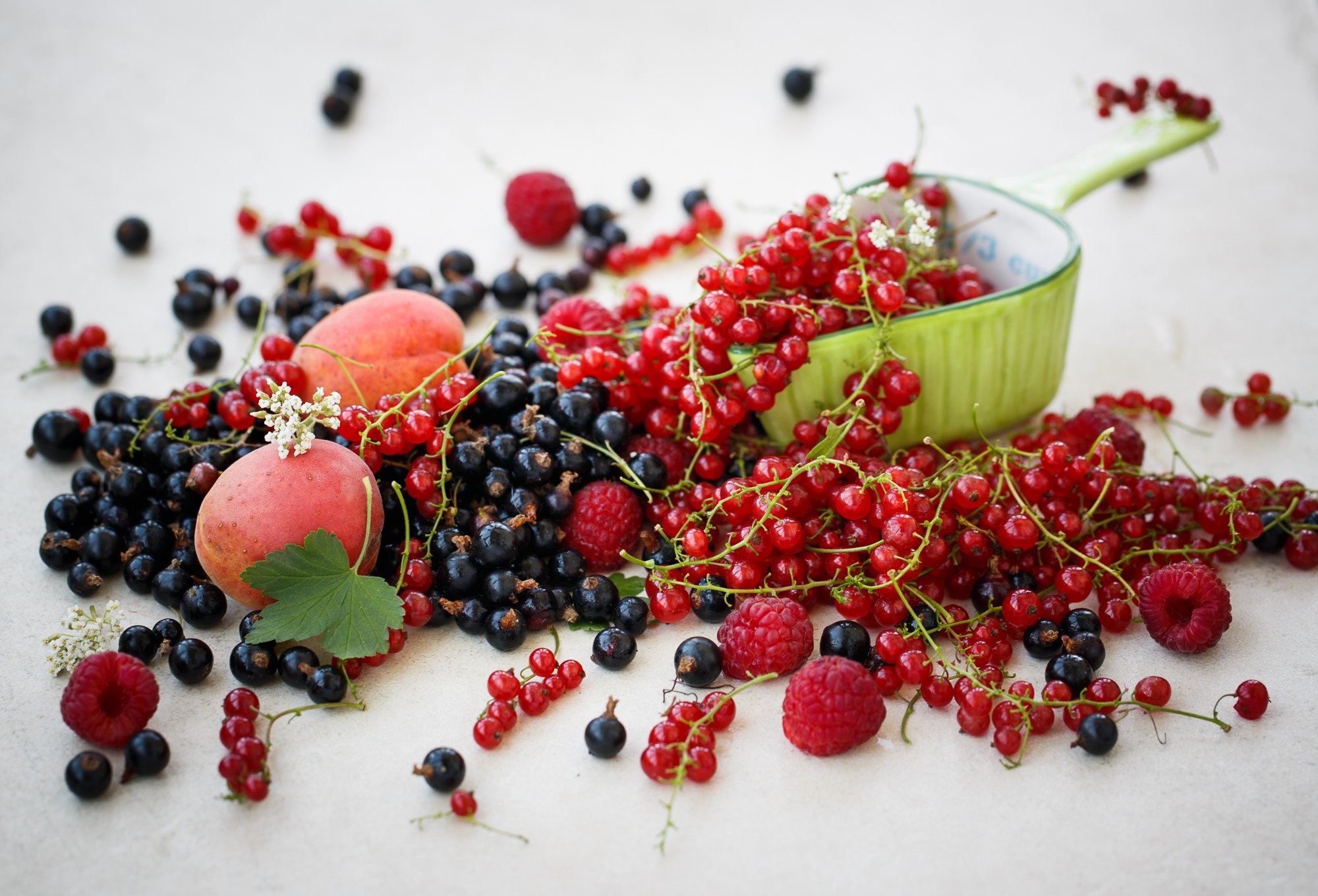 Fresh berries and peaches spilling from a green bowl HD Wallpaper