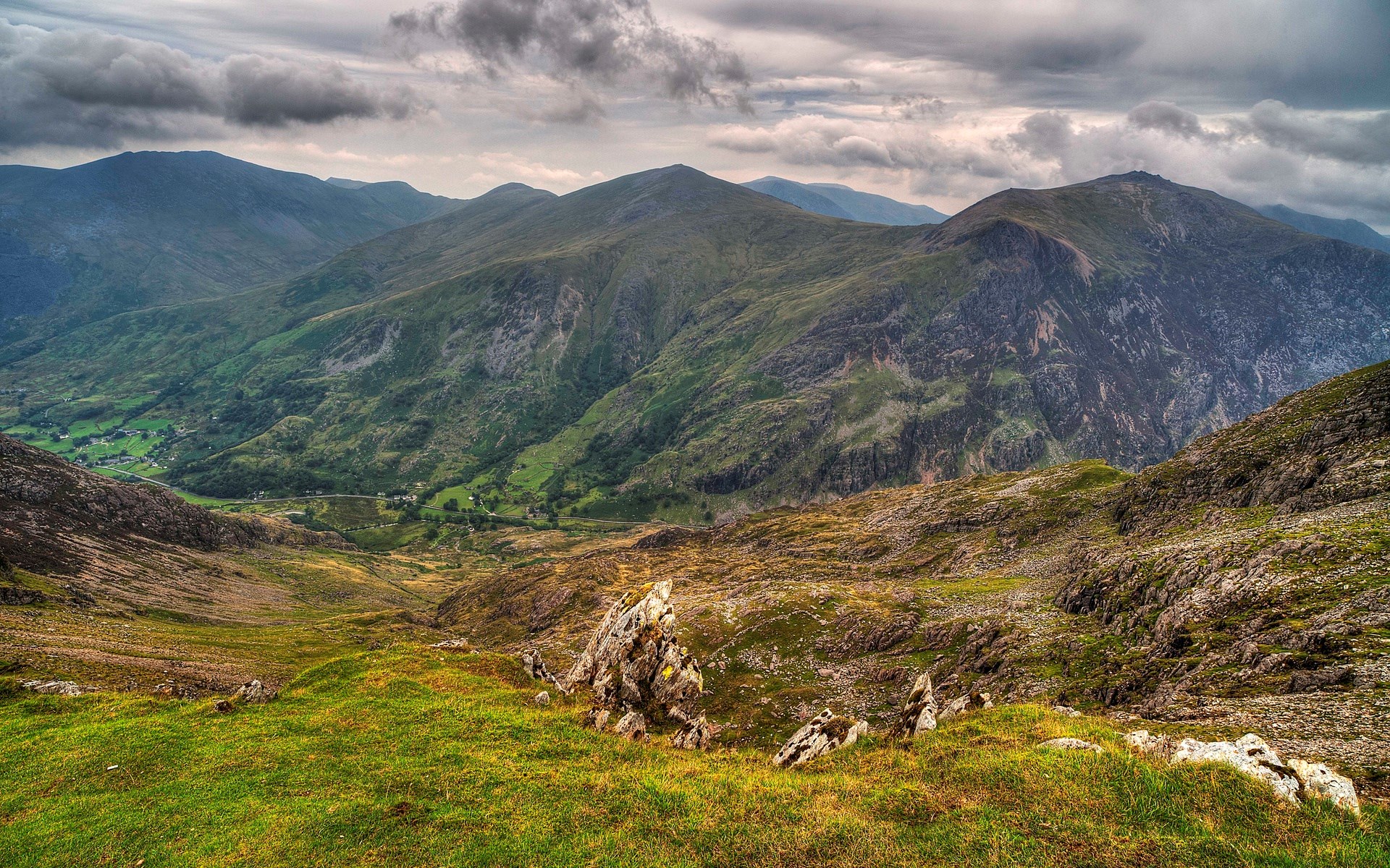 Mountain valley with green hills and rocky foreground HD Wallpaper