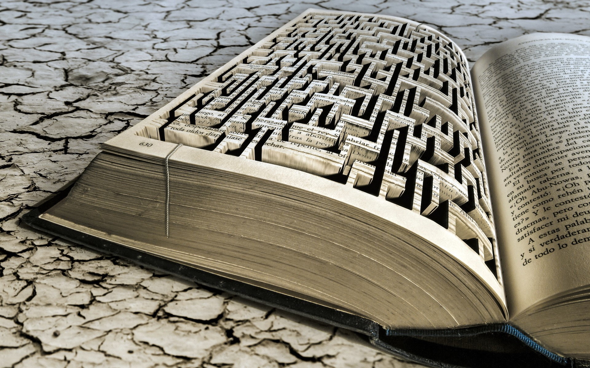 Book with maze carved into pages on cracked ground HD Wallpaper