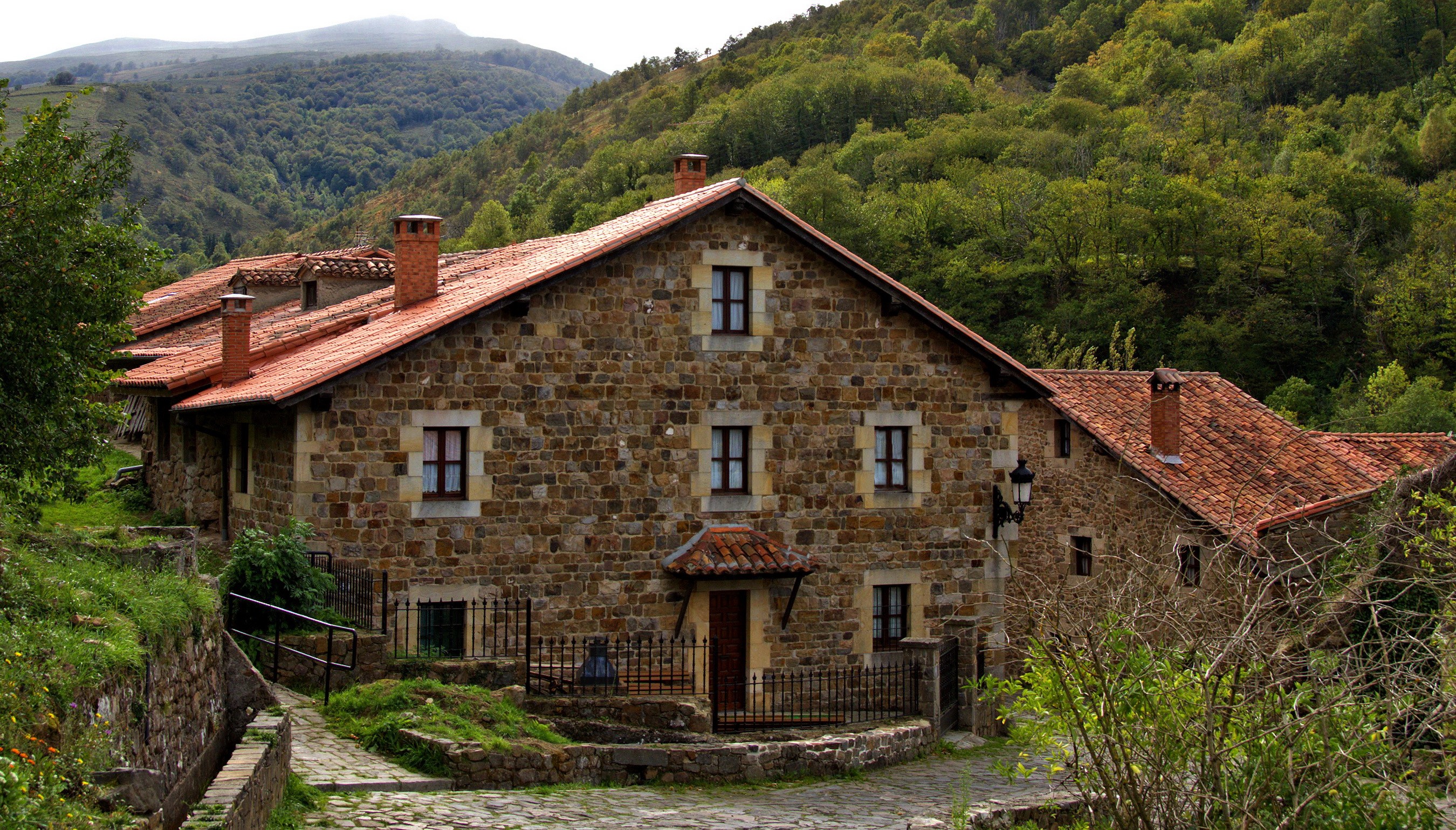 Stone houses with red tile roofs in a green mountainous landscape HD Wallpaper