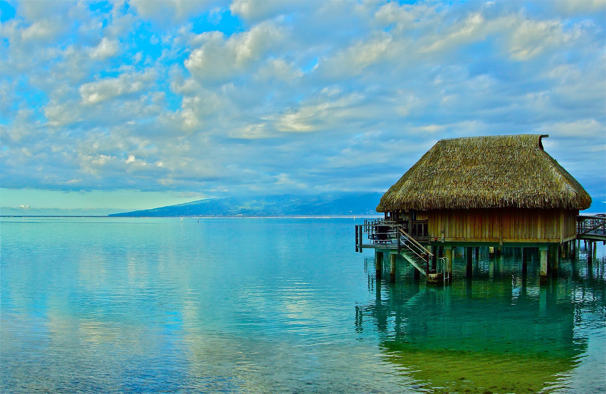 Overwater bungalow in French Polynesia with distant mountains HD Wallpaper