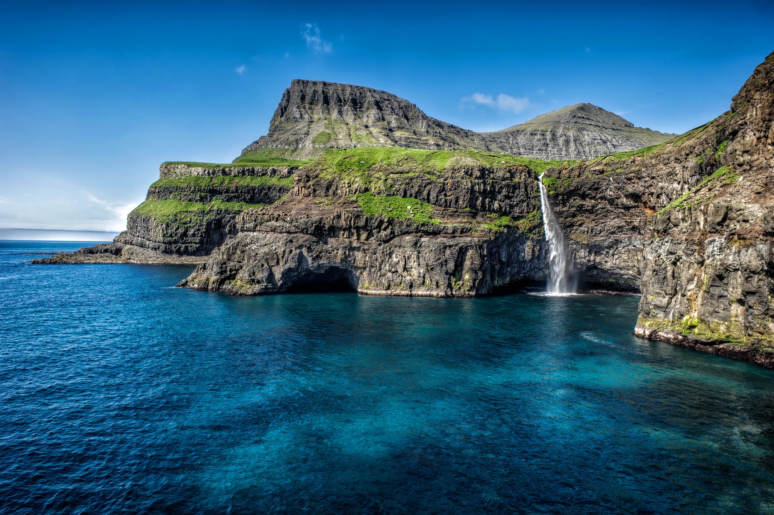 Waterfall cascading into the ocean from a rocky cliff HD Wallpaper