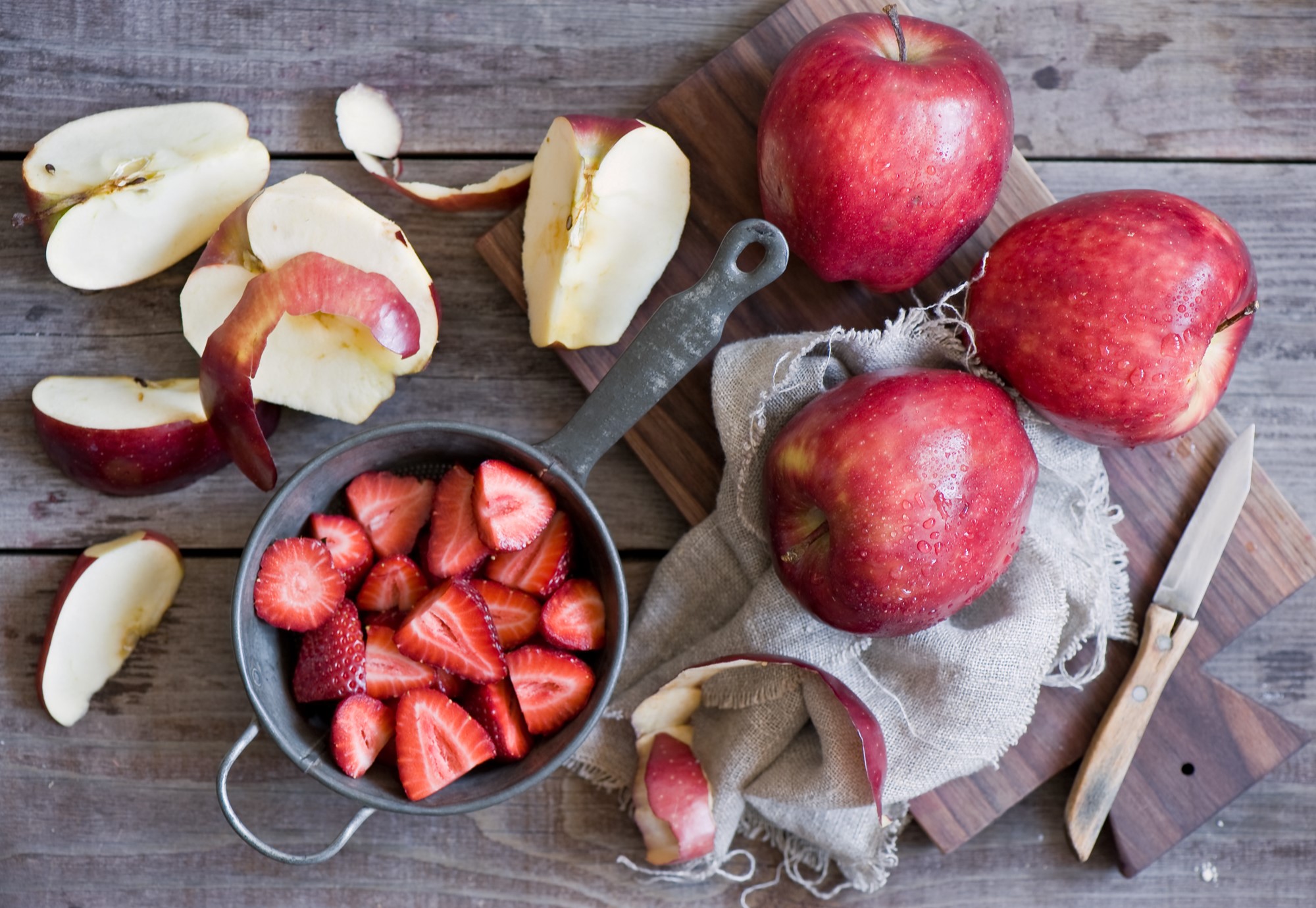 Apples and sliced strawberries on a wooden table HD Wallpaper