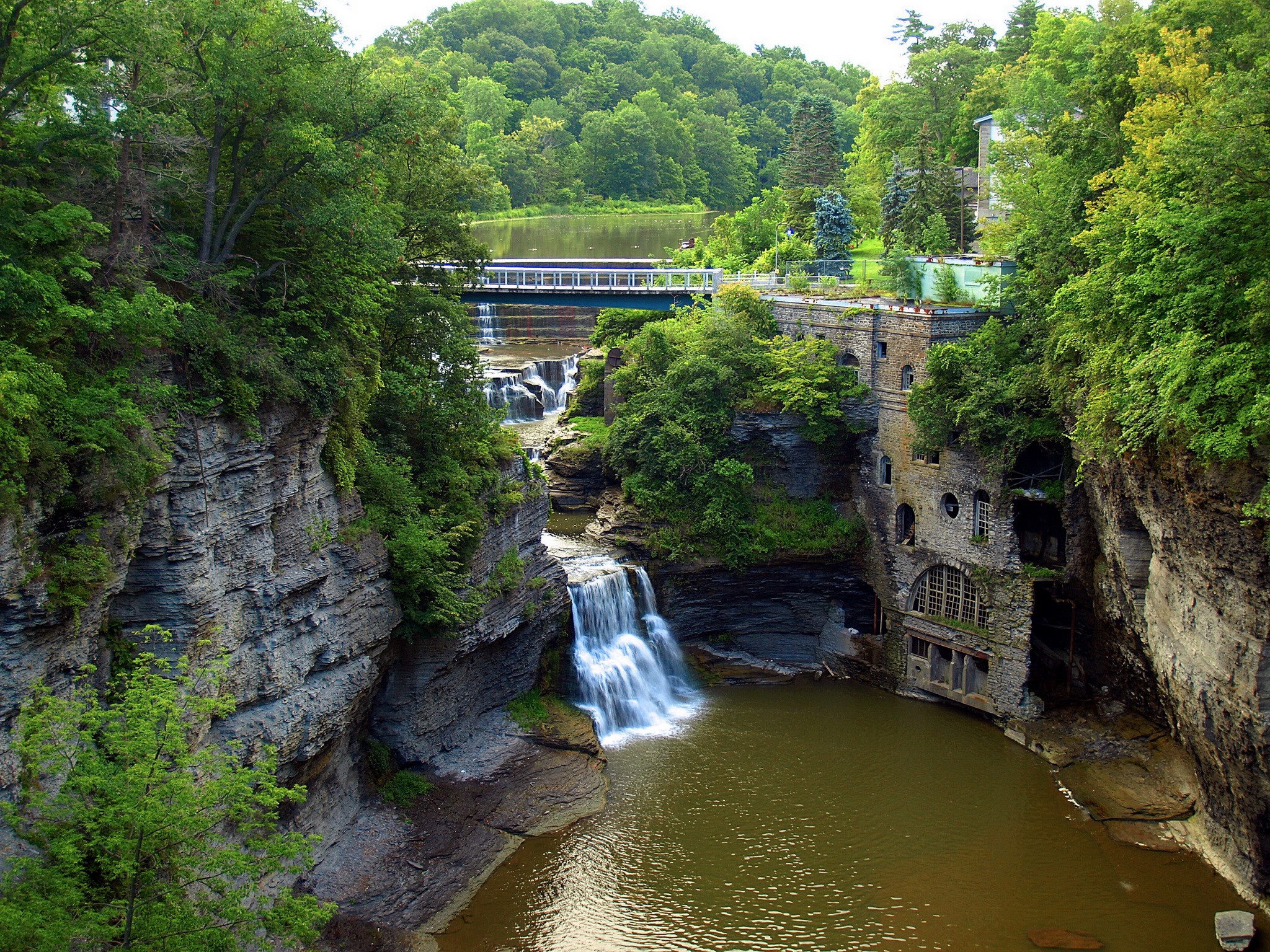 Waterfalls and an old stone building by a river HD Wallpaper