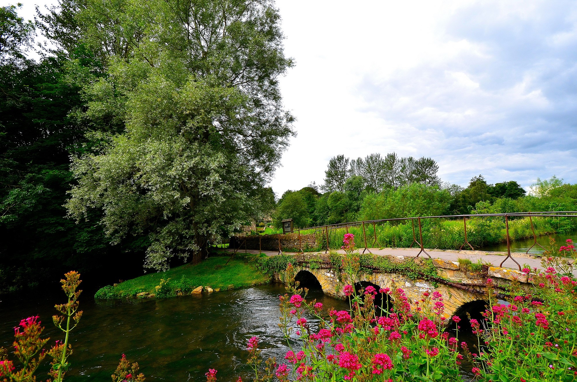 Stone bridge over a river in Bibury, England with trees and flowers HD Wallpaper