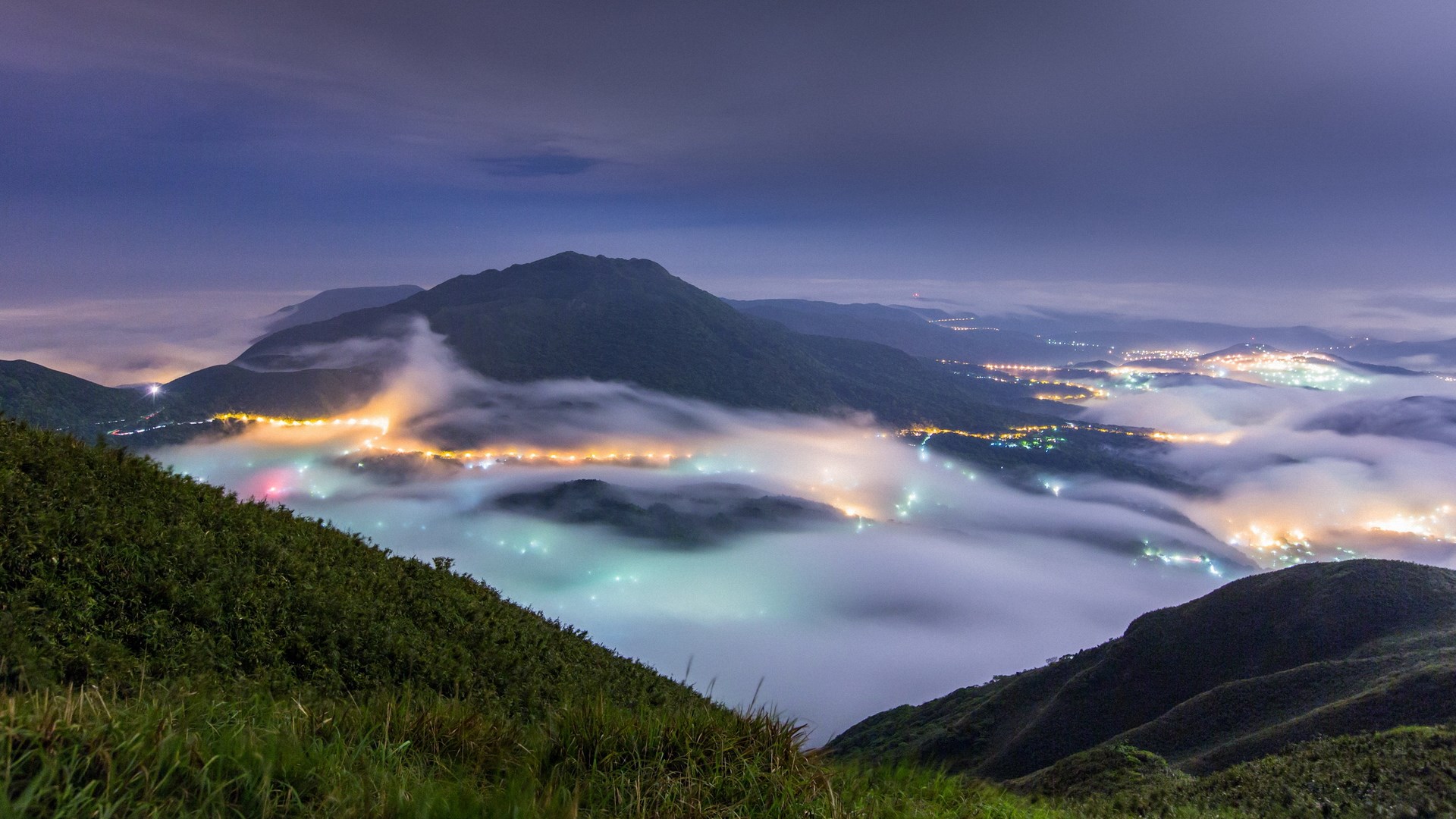 Mountain landscape with fog and city lights at night HD Wallpaper