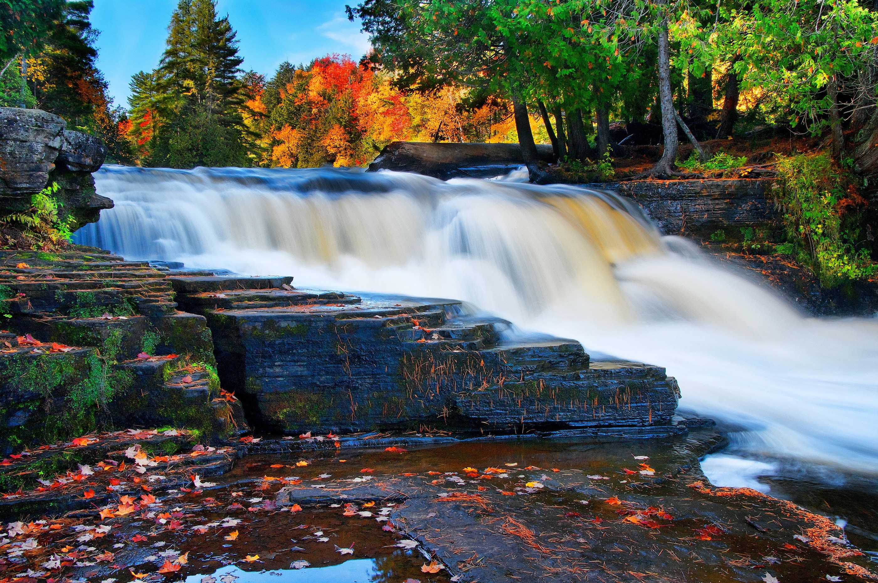 Waterfall cascading over layered stones in autumn forest HD Wallpaper