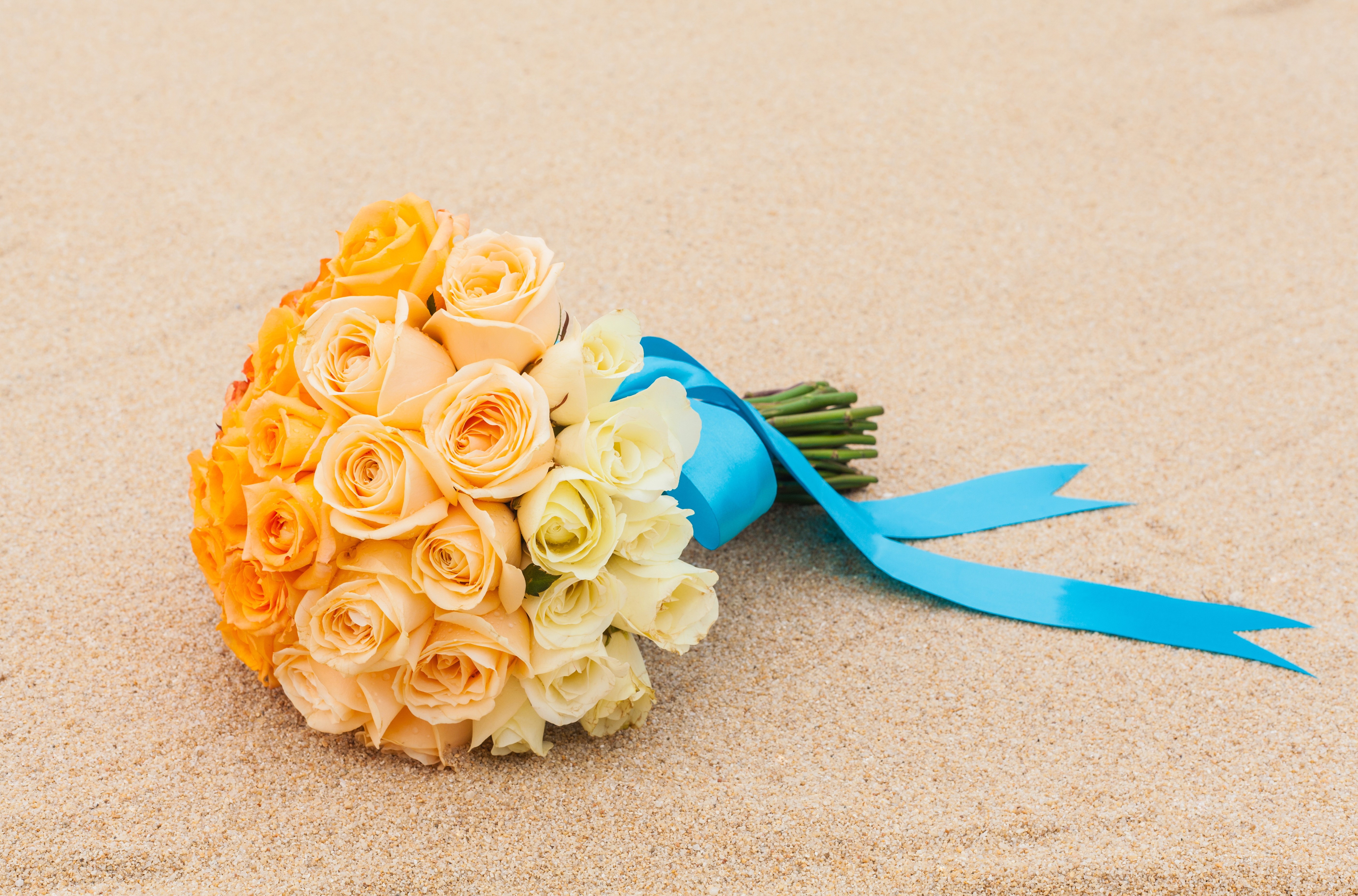 Bouquet of orange and yellow roses with blue ribbon on sand HD Wallpaper