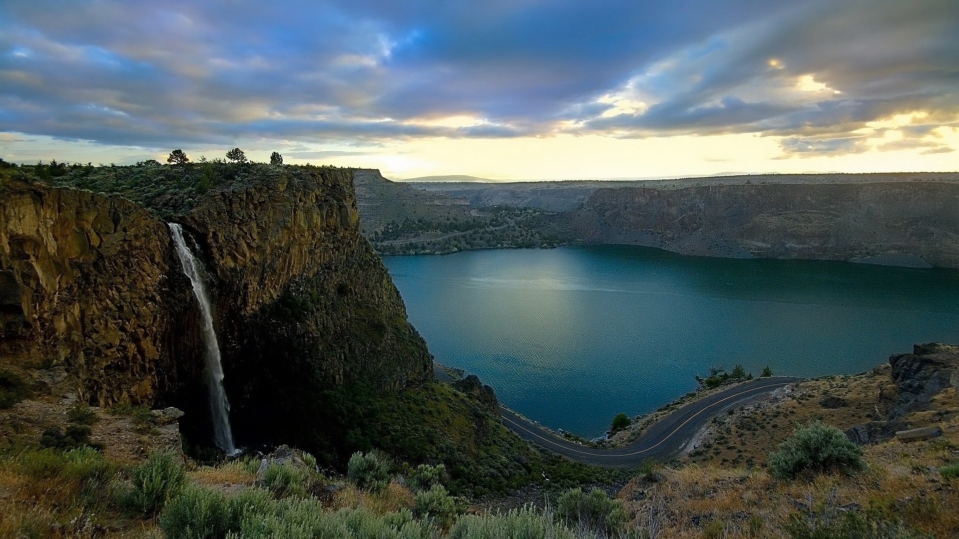 Waterfall cascading into a lake with a road HD Wallpaper