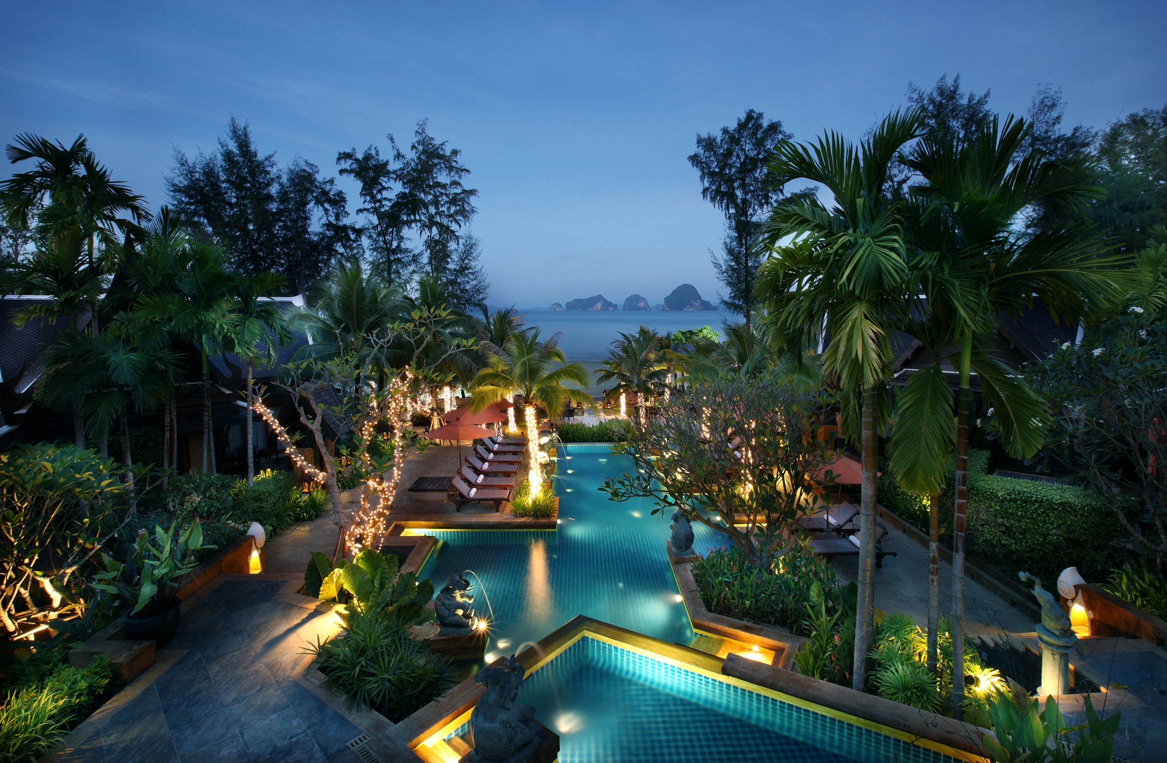 Tropical resort pool at night with palm trees and ocean view HD Wallpaper