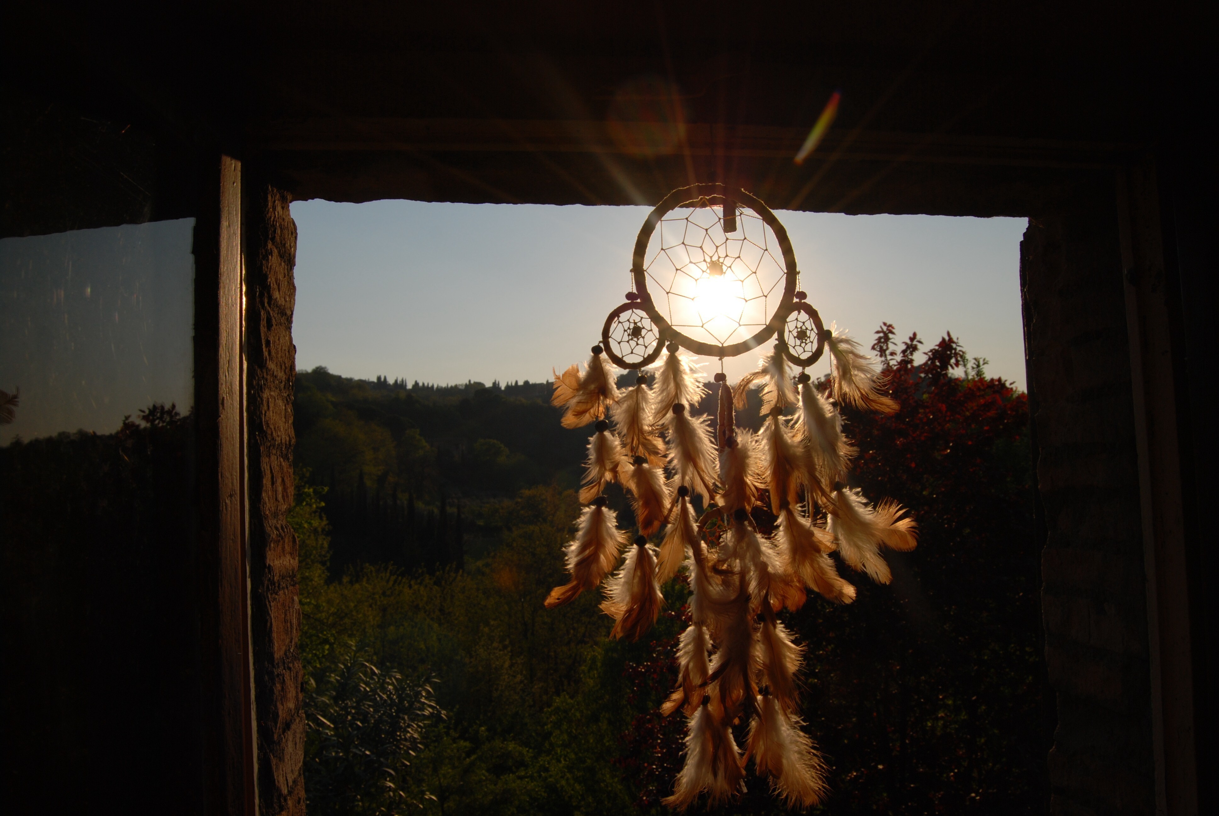 Dreamcatcher with feathers hanging in a window at sunset HD Wallpaper