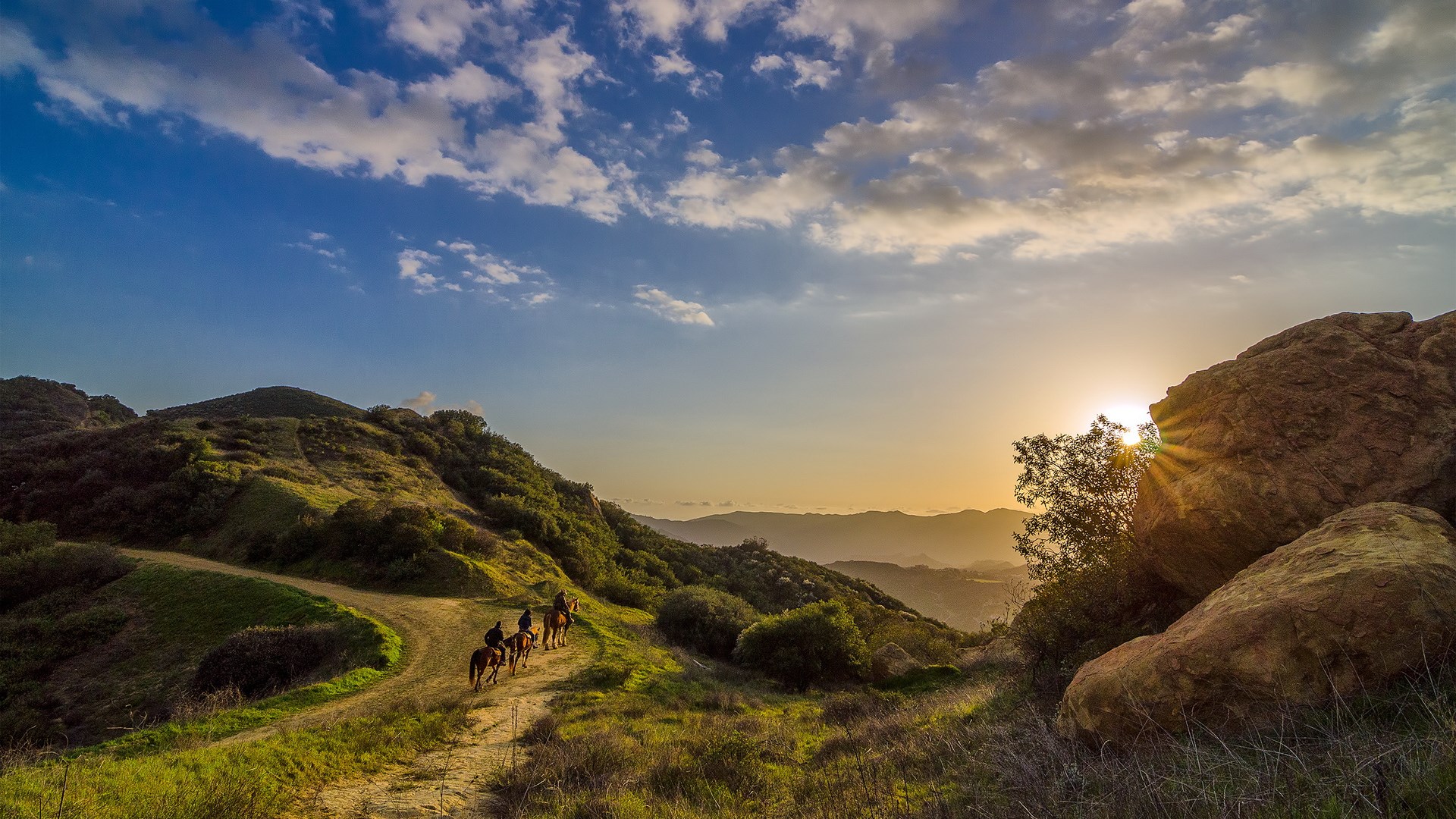 People riding horses on a mountain trail at sunset HD Wallpaper