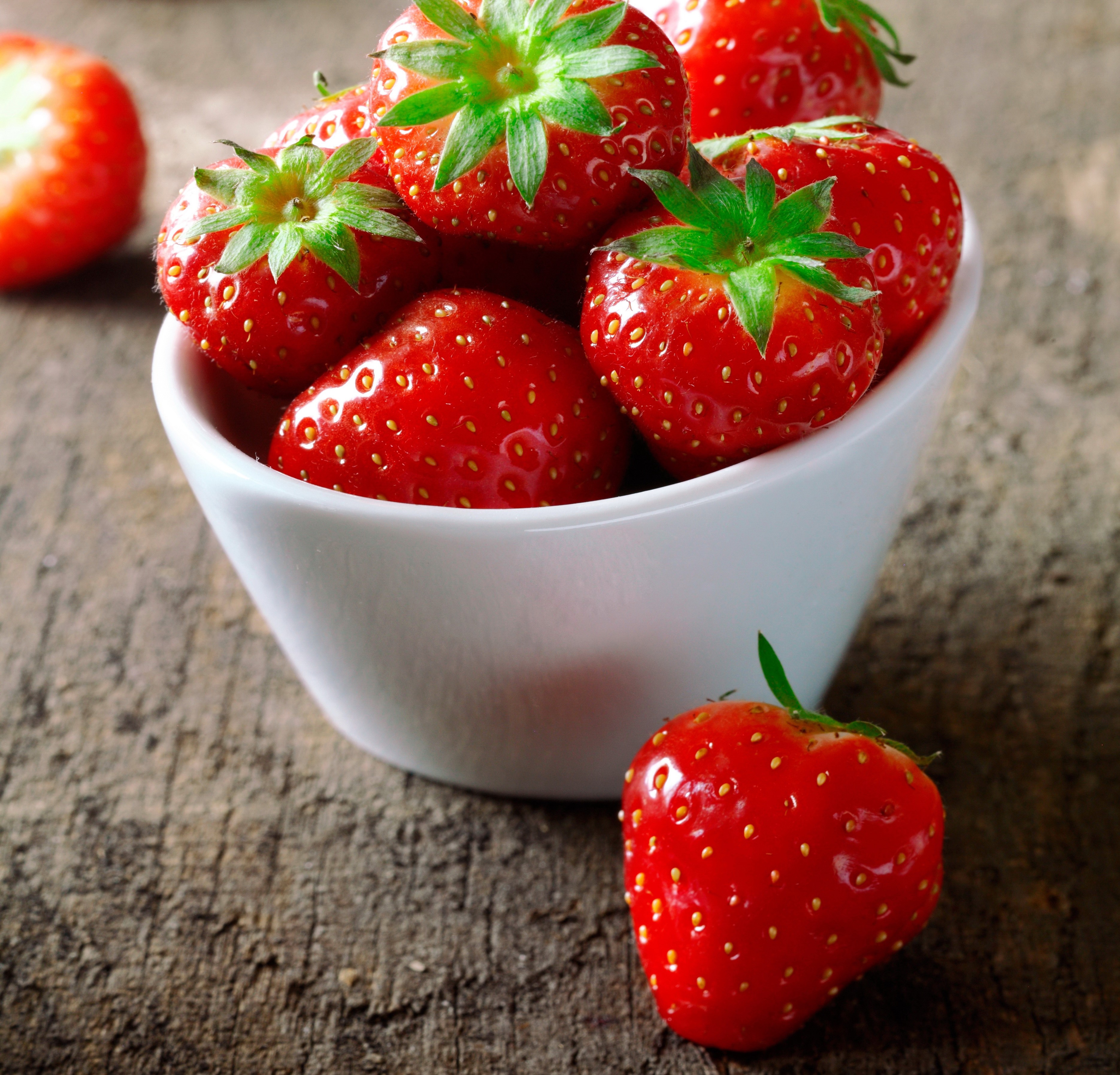 Strawberries in a white bowl on a wooden surface HD Wallpaper