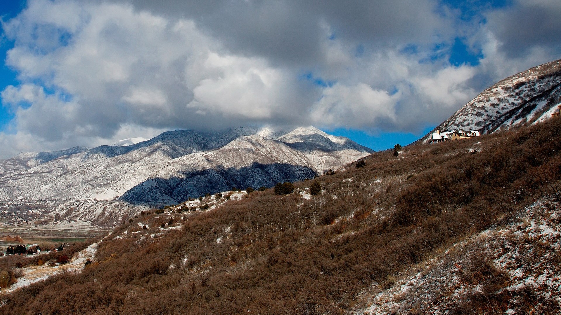 Snow-dusted mountains under cloudy sky with houses on a slope HD Wallpaper
