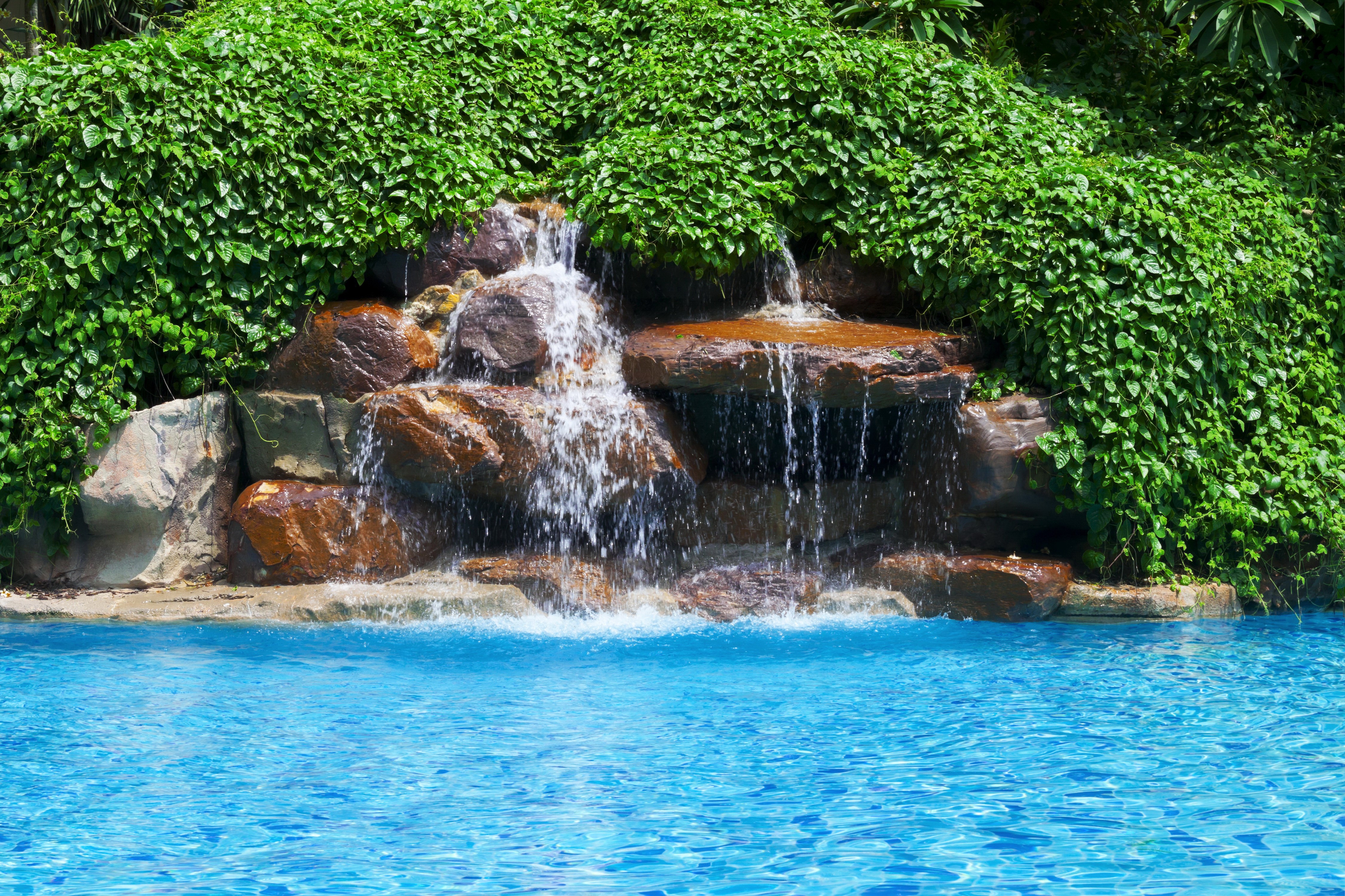 Waterfall cascading into a swimming pool HD Wallpaper