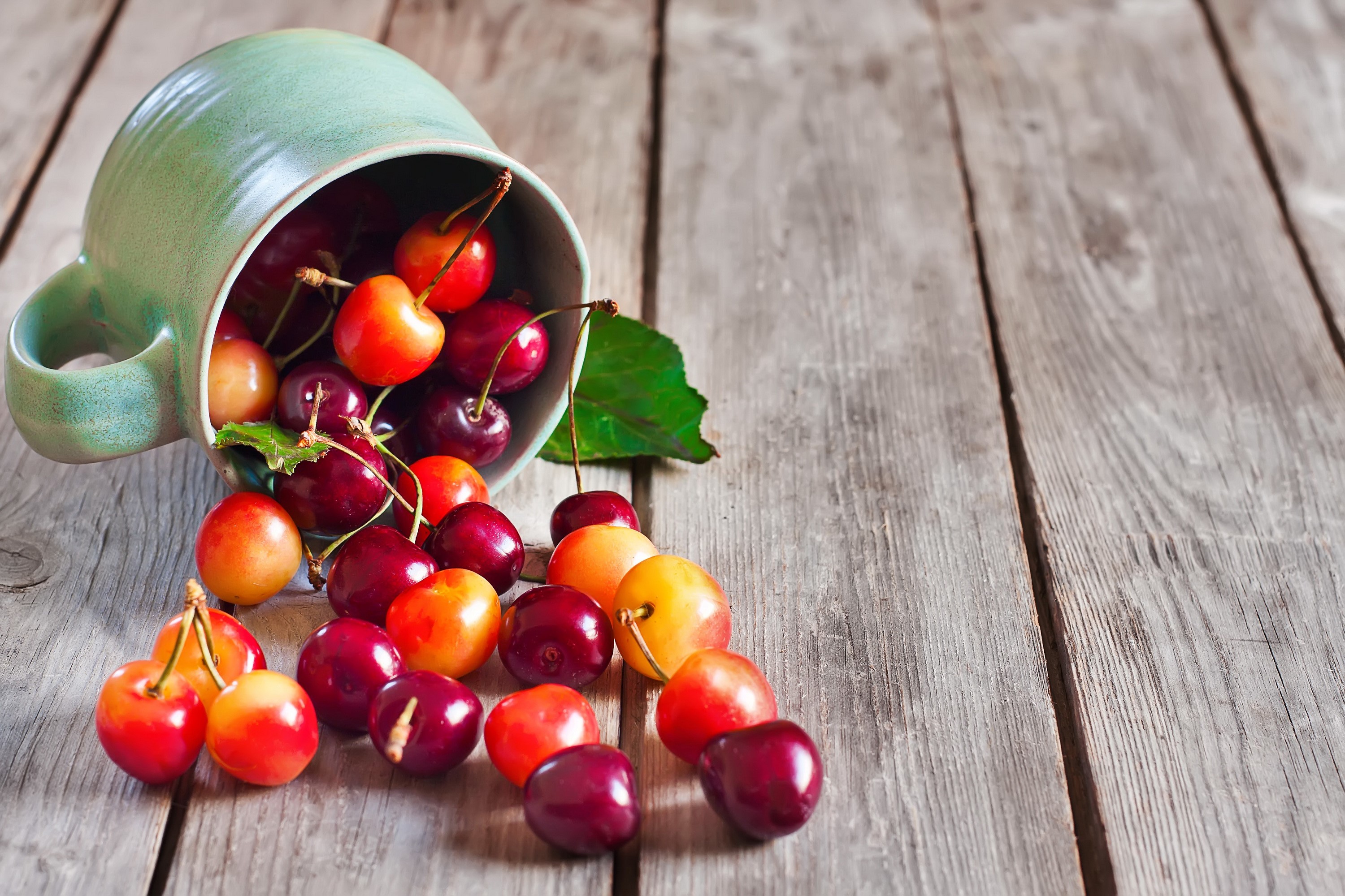 Cherries spilling from a mug onto a wooden table HD Wallpaper