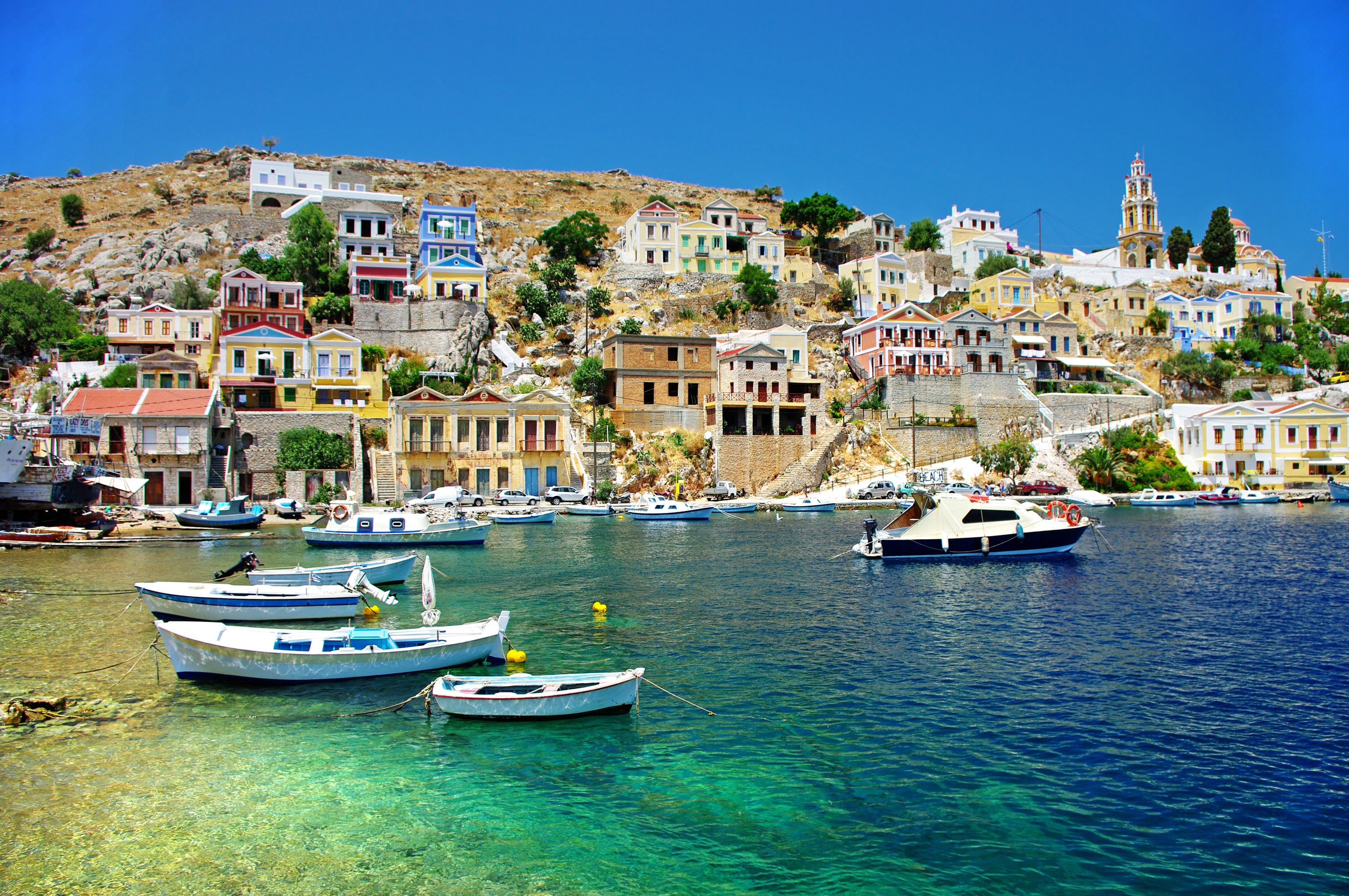 Colorful houses on a hill overlooking a harbor with boats in Greece HD Wallpaper