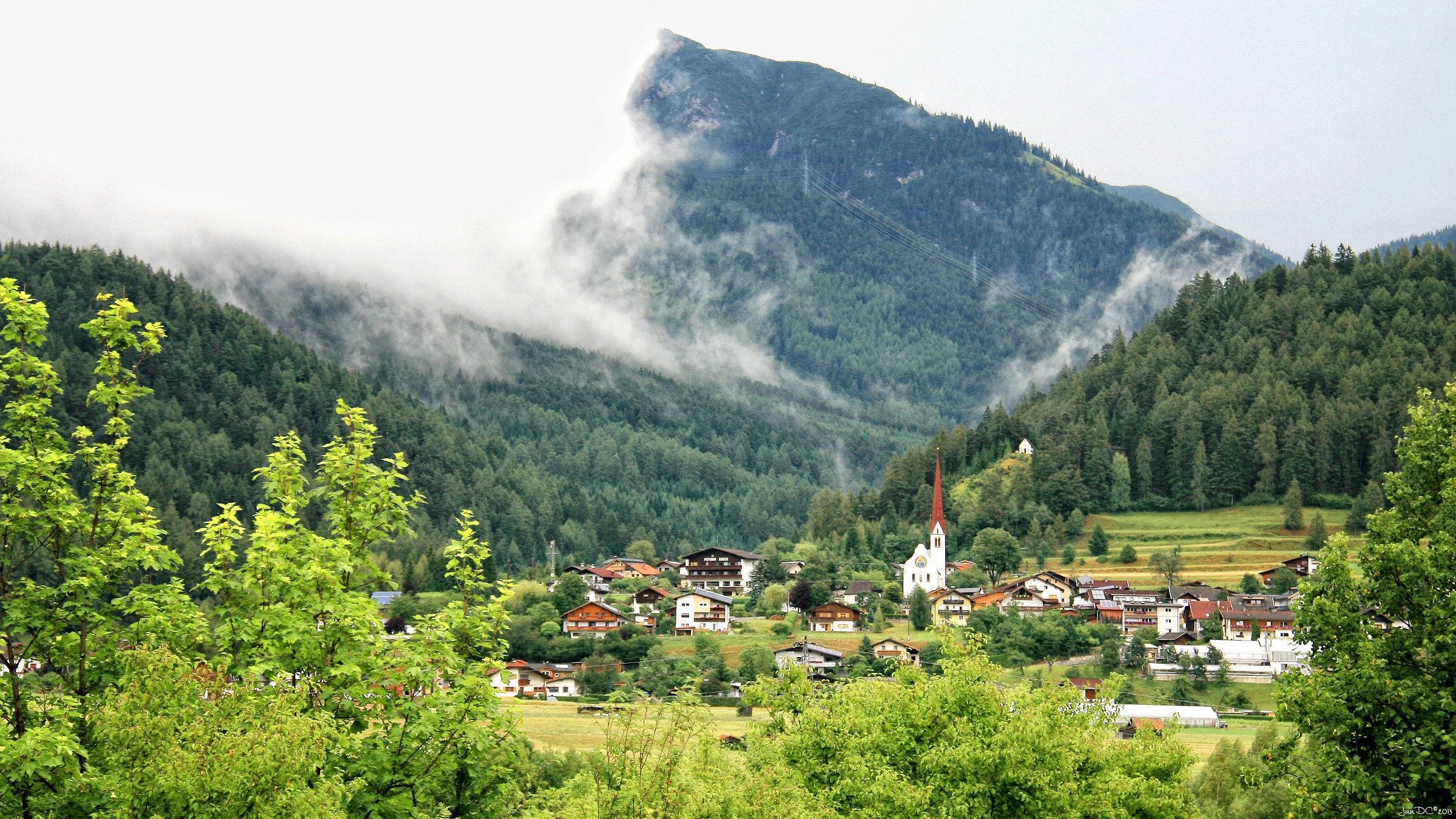 Village nestled in a mountain valley with fog HD Wallpaper