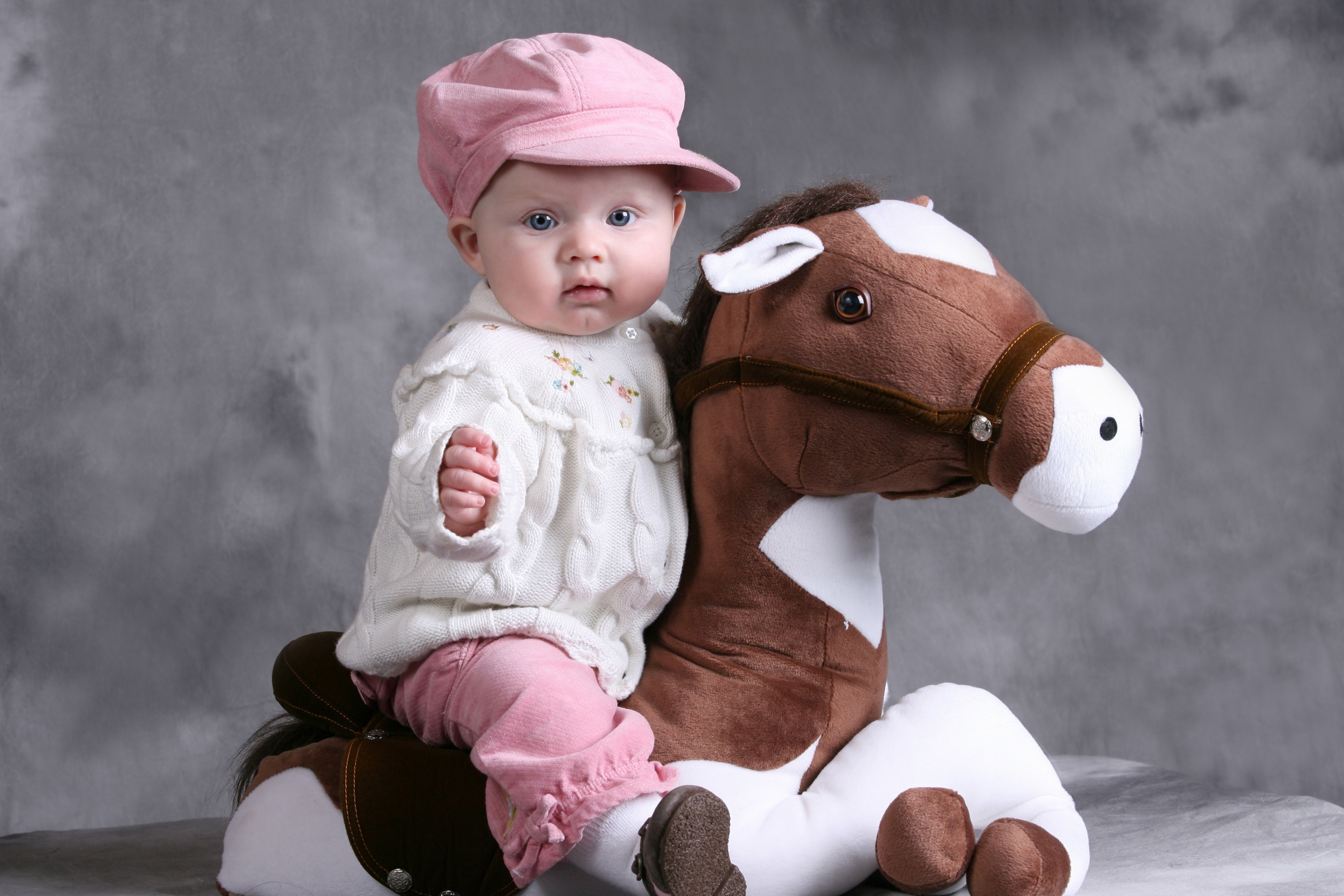 Baby girl in pink hat on toy horse HD Wallpaper