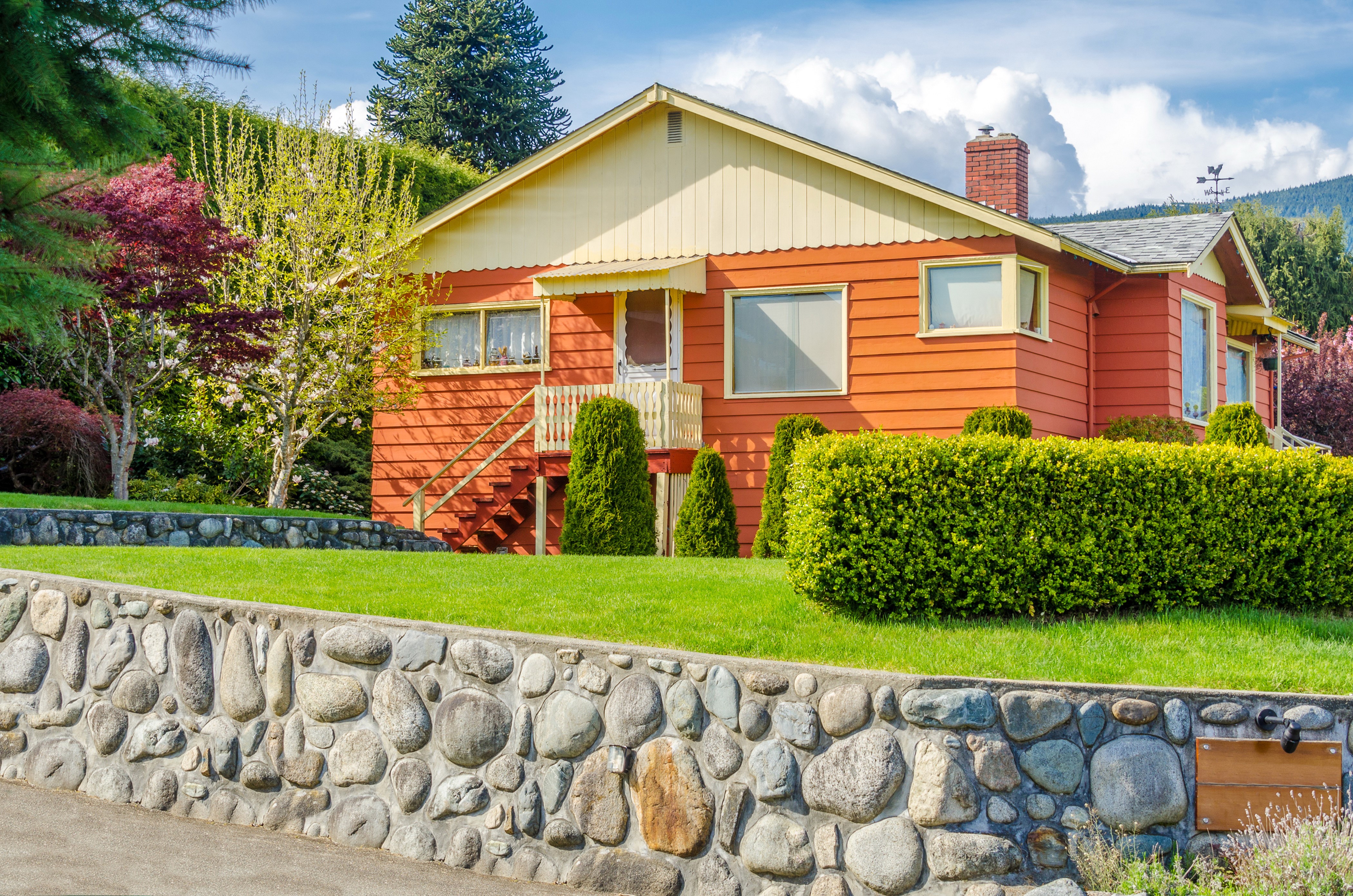 Orange house with stone wall and lawn HD Wallpaper