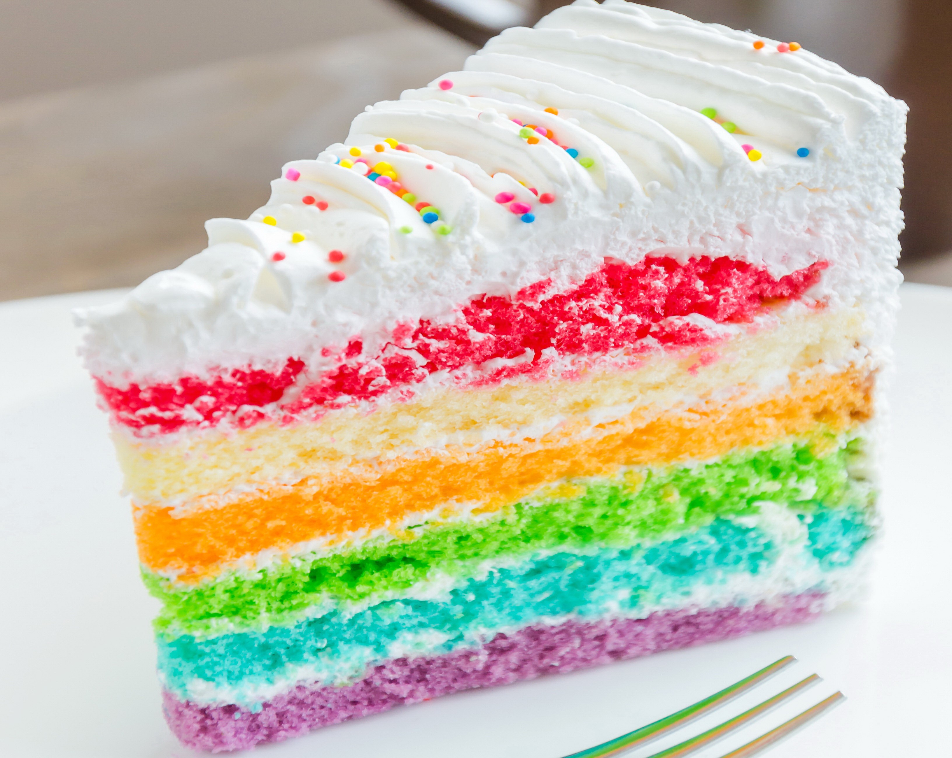 Slice of rainbow cake with white frosting and sprinkles HD Wallpaper