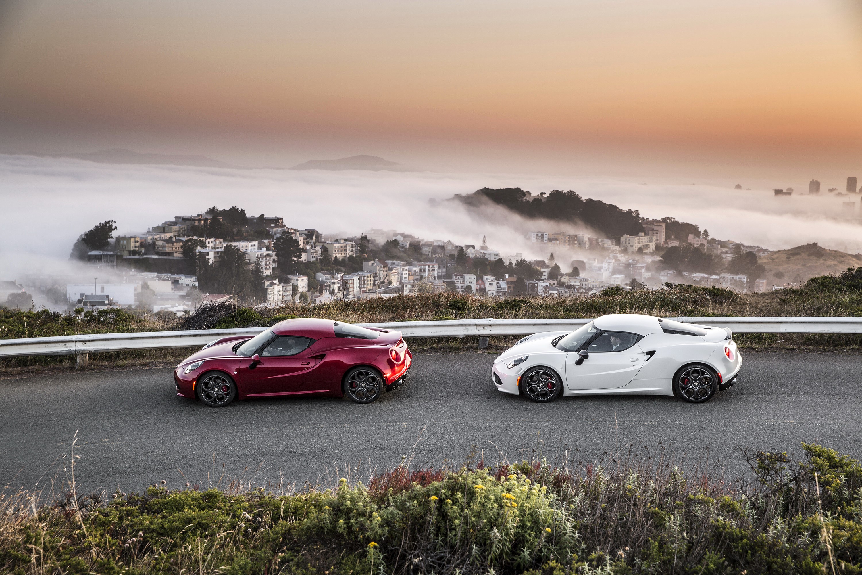 Two Alfa Romeo 4C cars on a road with fog and city in background HD Wallpaper