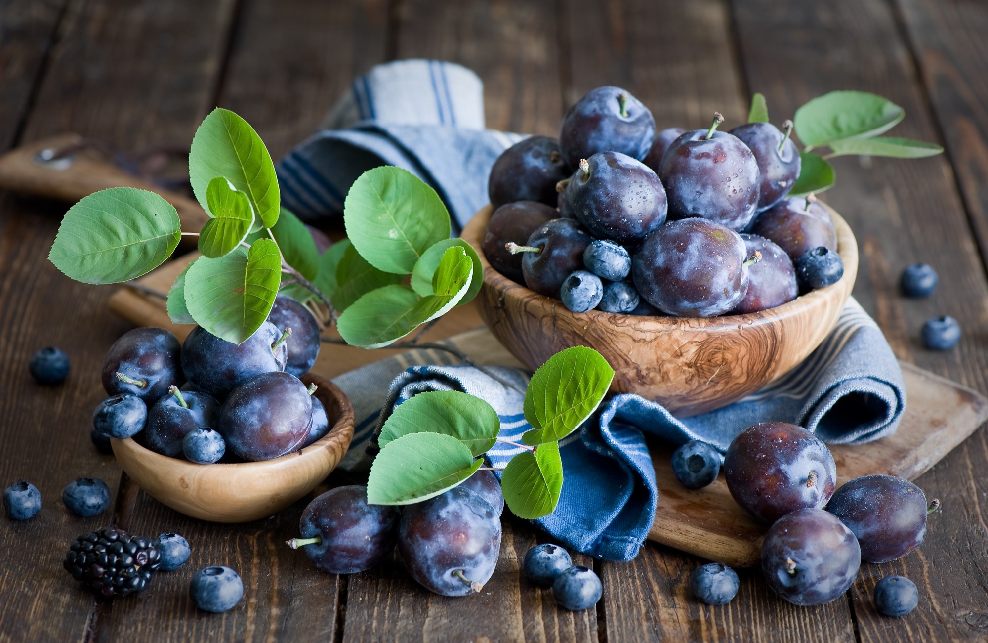 Plums and blueberries in wooden bowls on a rustic table HD Wallpaper
