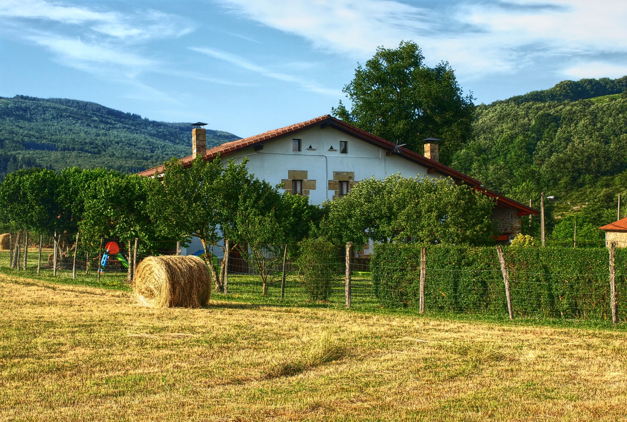 House in a field with hay bales and trees HD Wallpaper