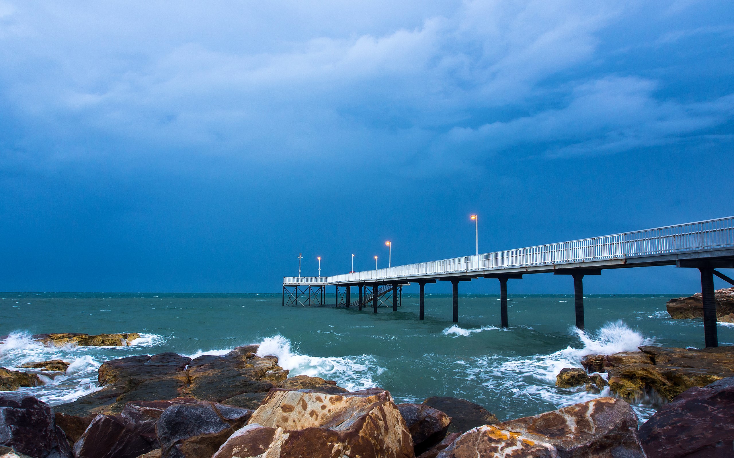 Pier over the ocean with rocks and stormy sky HD Wallpaper