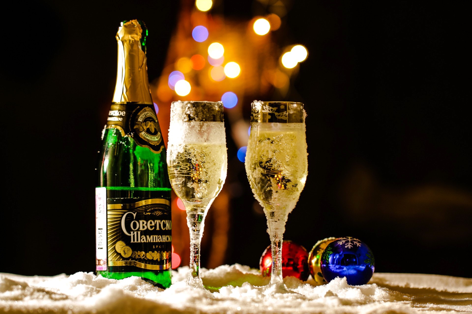 Champagne bottle and glasses in snow with Christmas lights HD Wallpaper
