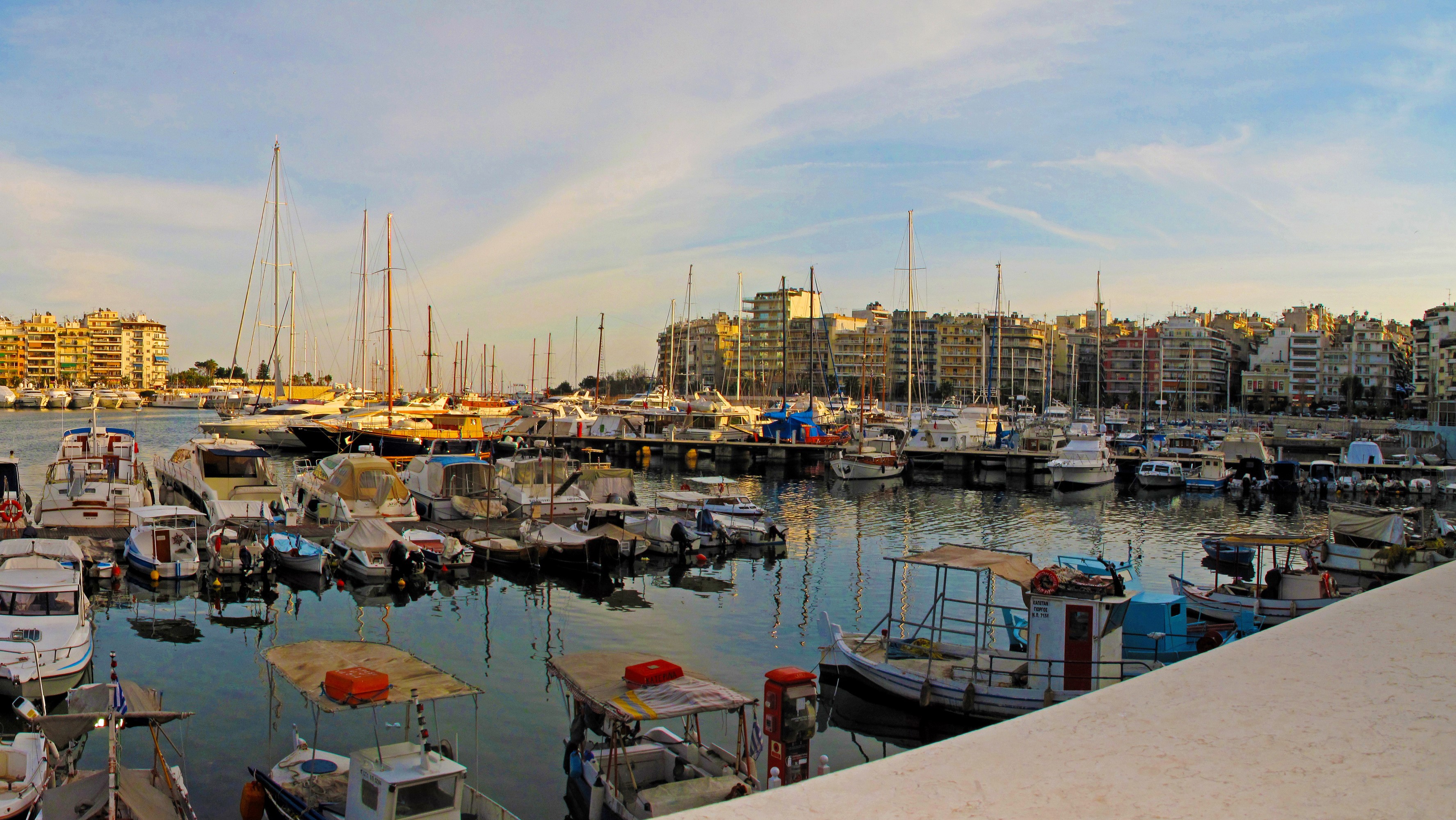 Boats docked in a marina with buildings in the background in Piraeus, Greece HD Wallpaper