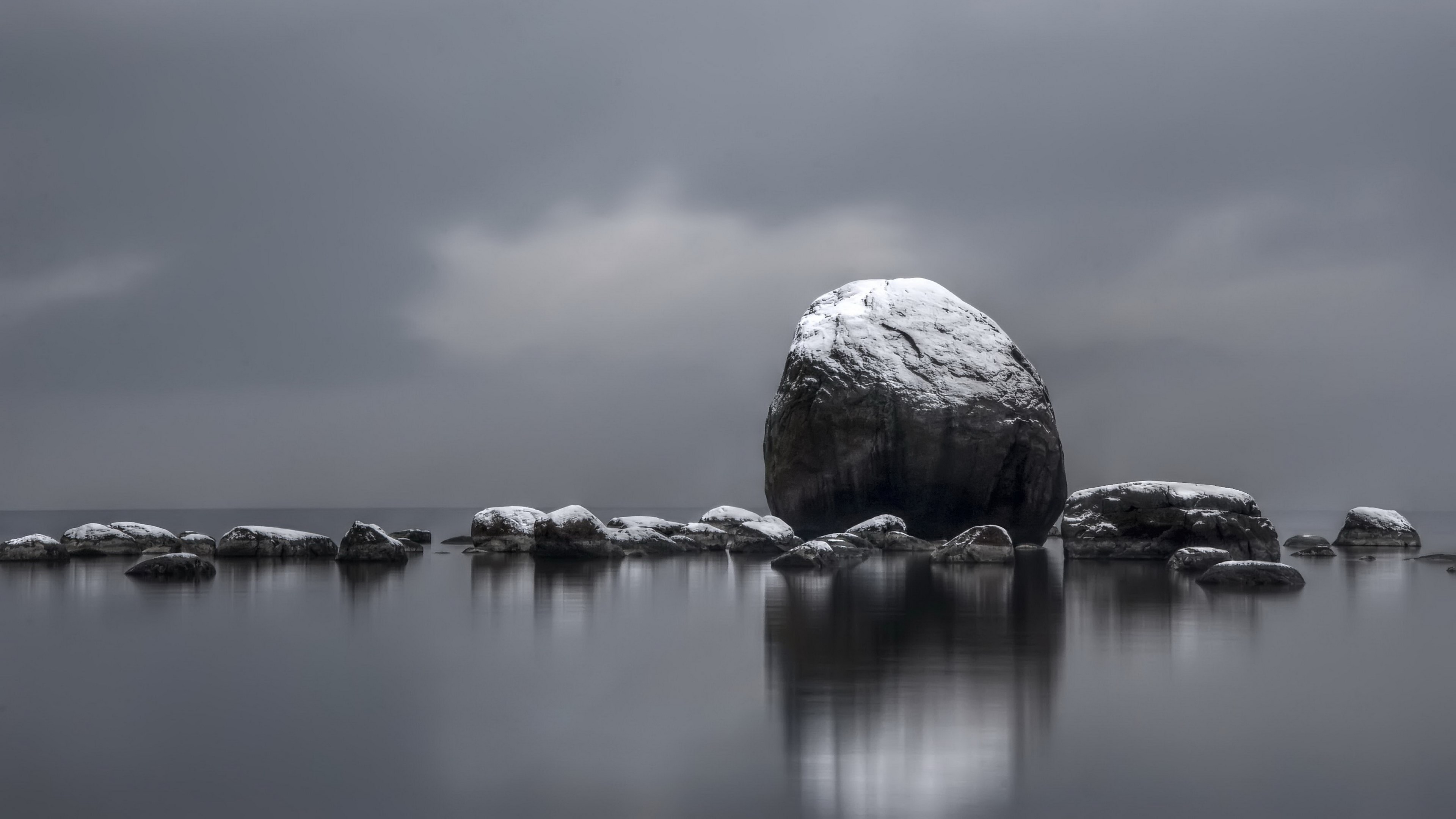 Snow-covered rocks in calm water under cloudy sky HD Wallpaper