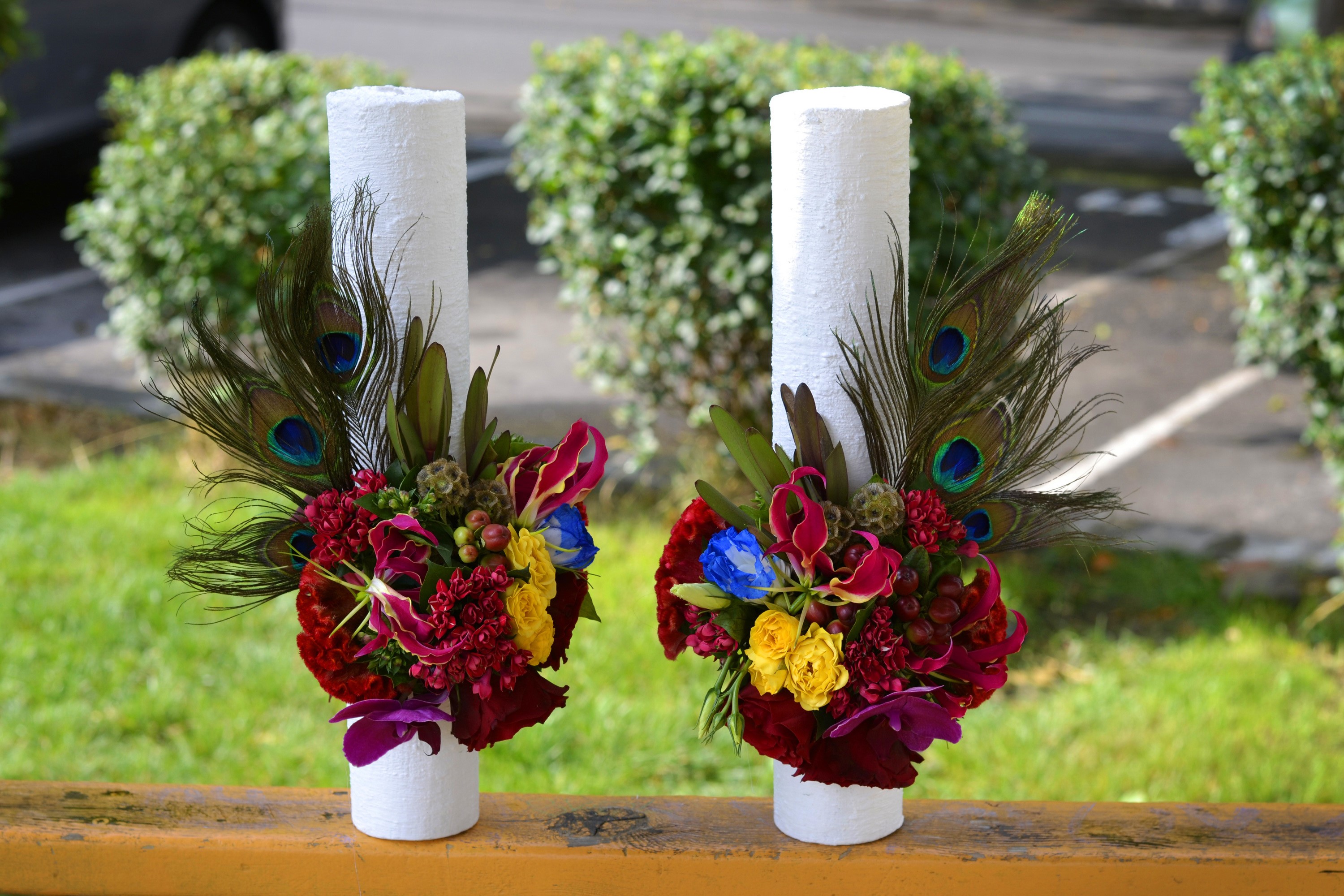 Two white pillar candles decorated with peacock feathers and flowers HD Wallpaper