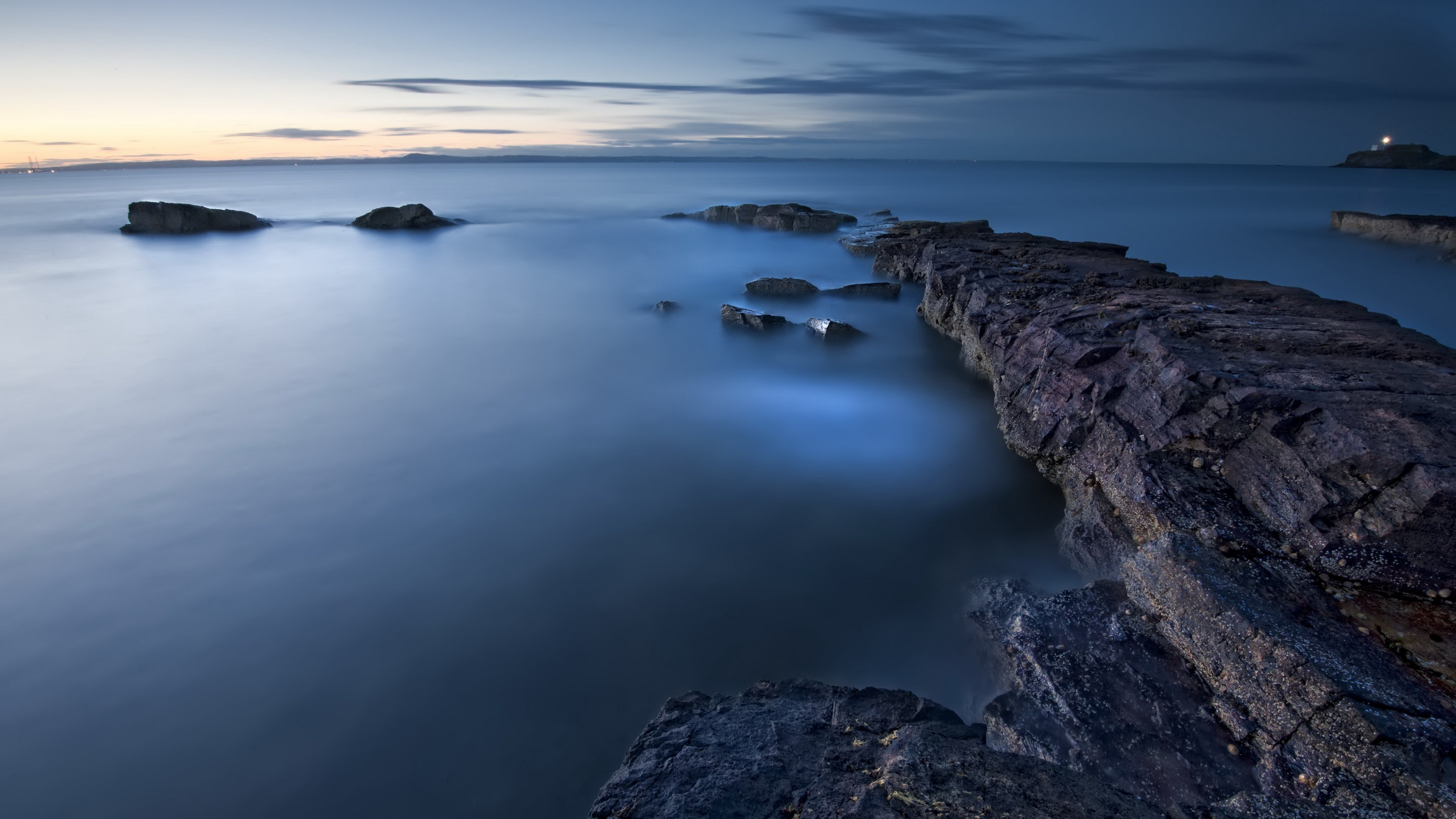 Rocky coastline at dusk with calm water HD Wallpaper