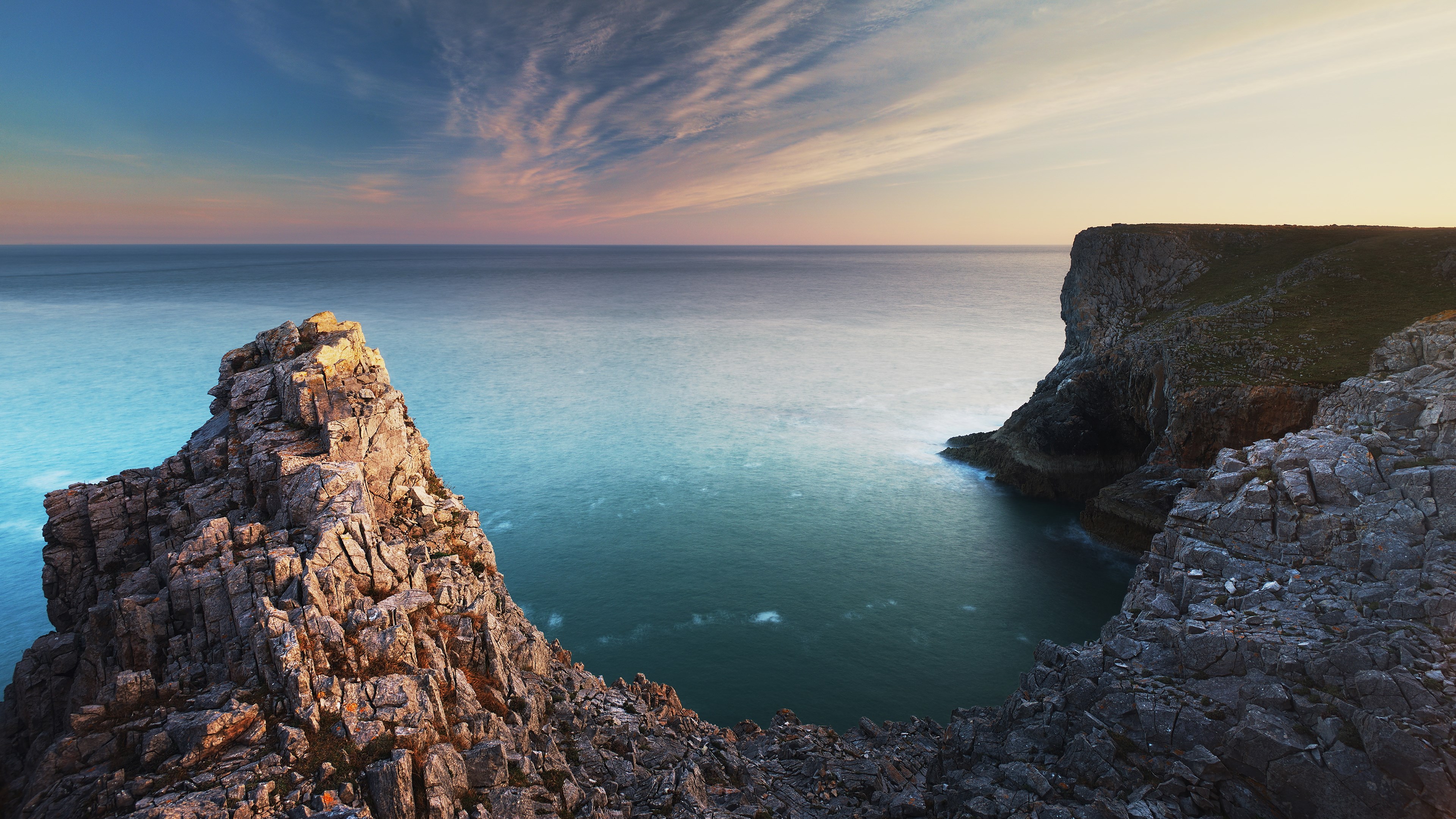 Rocky cliffs overlooking a calm sea at sunset HD Wallpaper